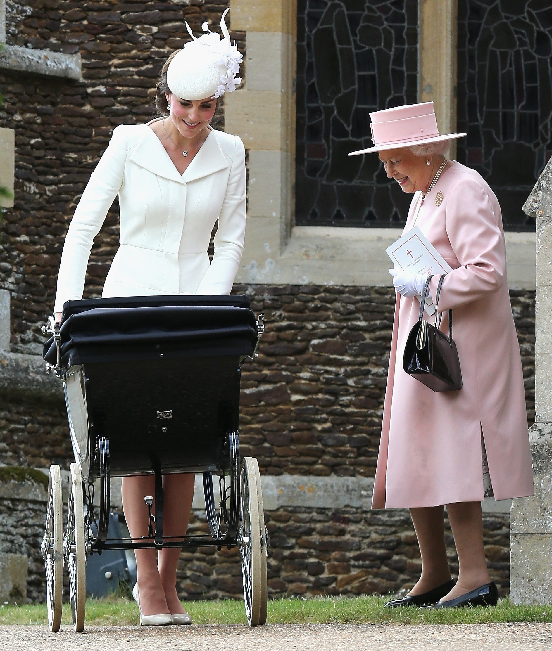 Kate Middleton schiebt ihre Tochter Prinzessin Charlotte im Kinderwagen, während Königin Elizabeth II. zusieht, wie sie die Kirche St. Mary Magdalene auf dem Sandringham Estate zur Taufe von Prinzessin Charlotte am 5. Juli 2015 in King's Lynn, England, verlassen | Quelle: Getty Images