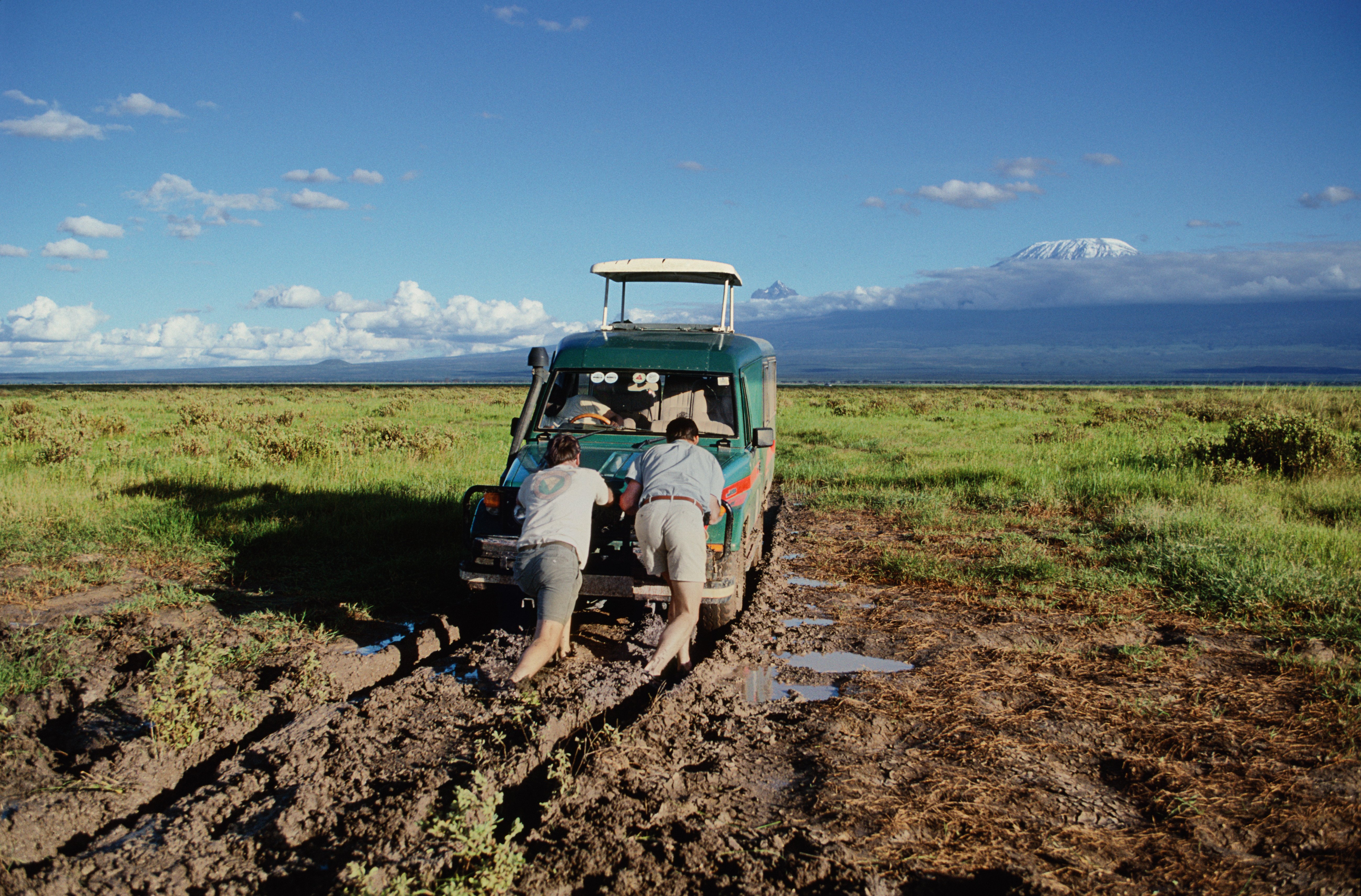 Two men pushing vehicle out of mud, rear view | Photo : Getty Images