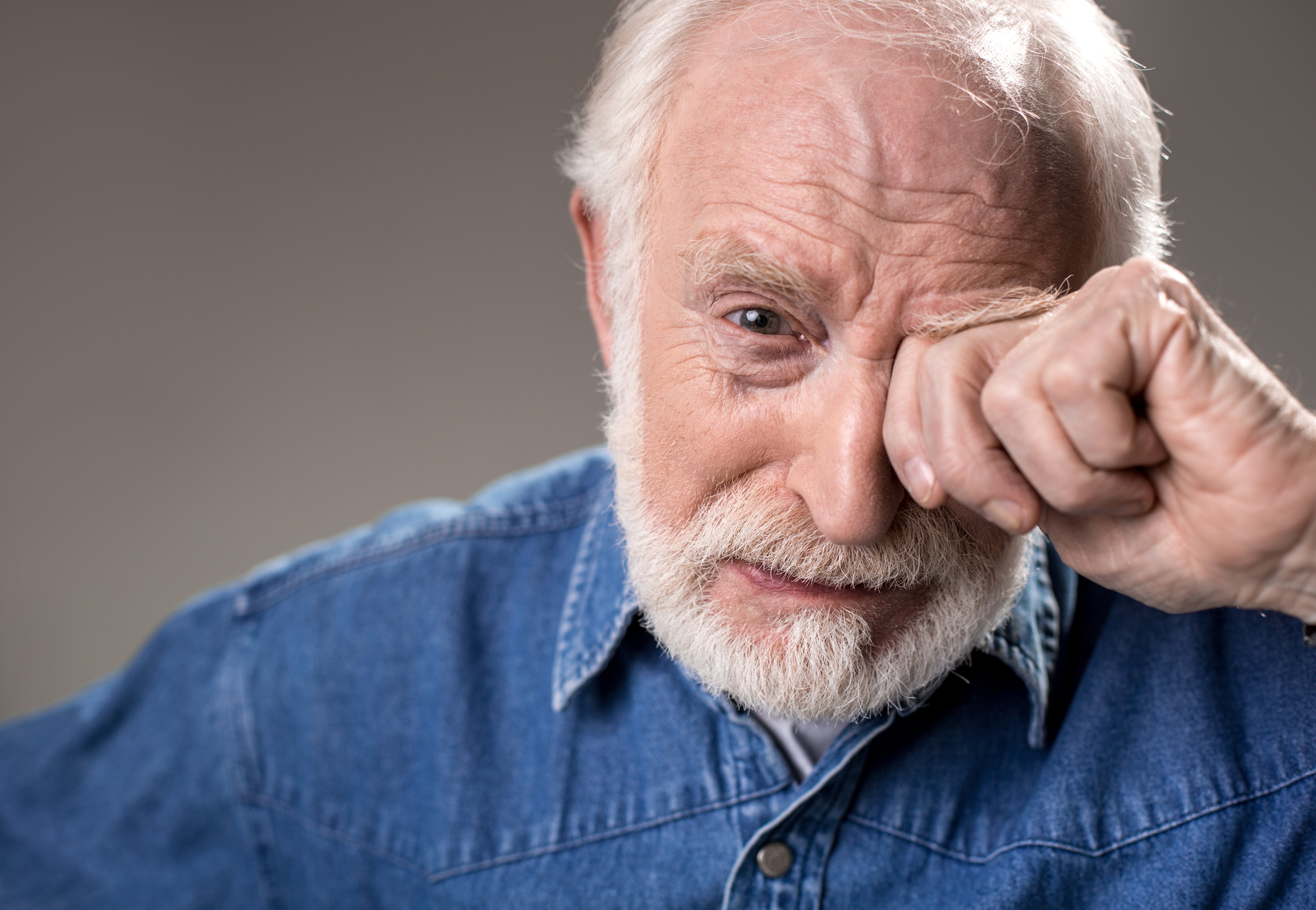 Older man in blue shirt covering one eye as he cries.|Source: Shutterstock