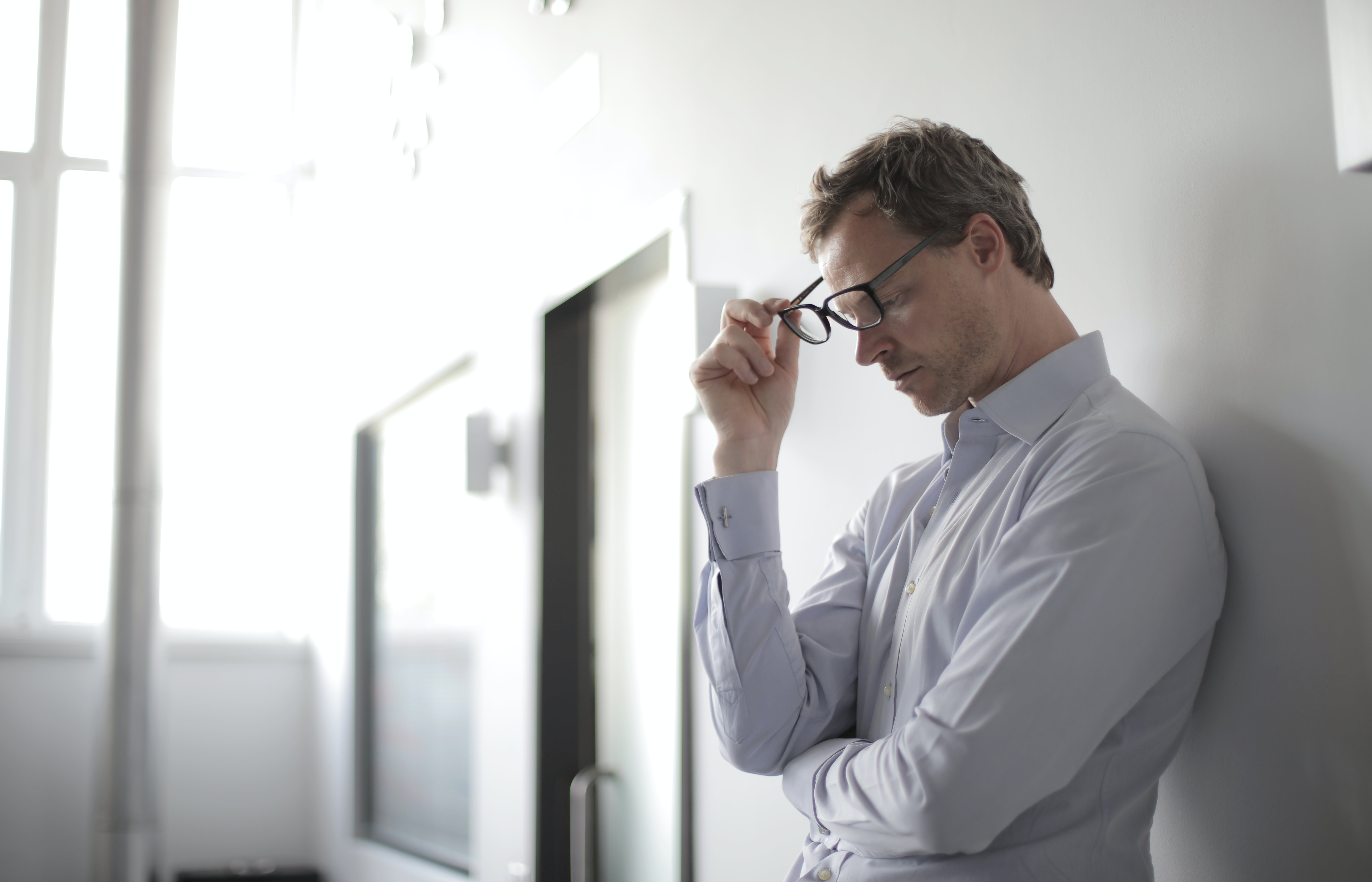 An upset man holding his glasses while standing against a wall | Source: Pexels