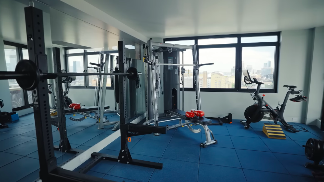The gym looks more like a private training studio than a token exercise corner. Weights, machines and a Peloton fill the room, while the mirrored wall makes it feel even larger. | Source: YouTube/Architectural Digest