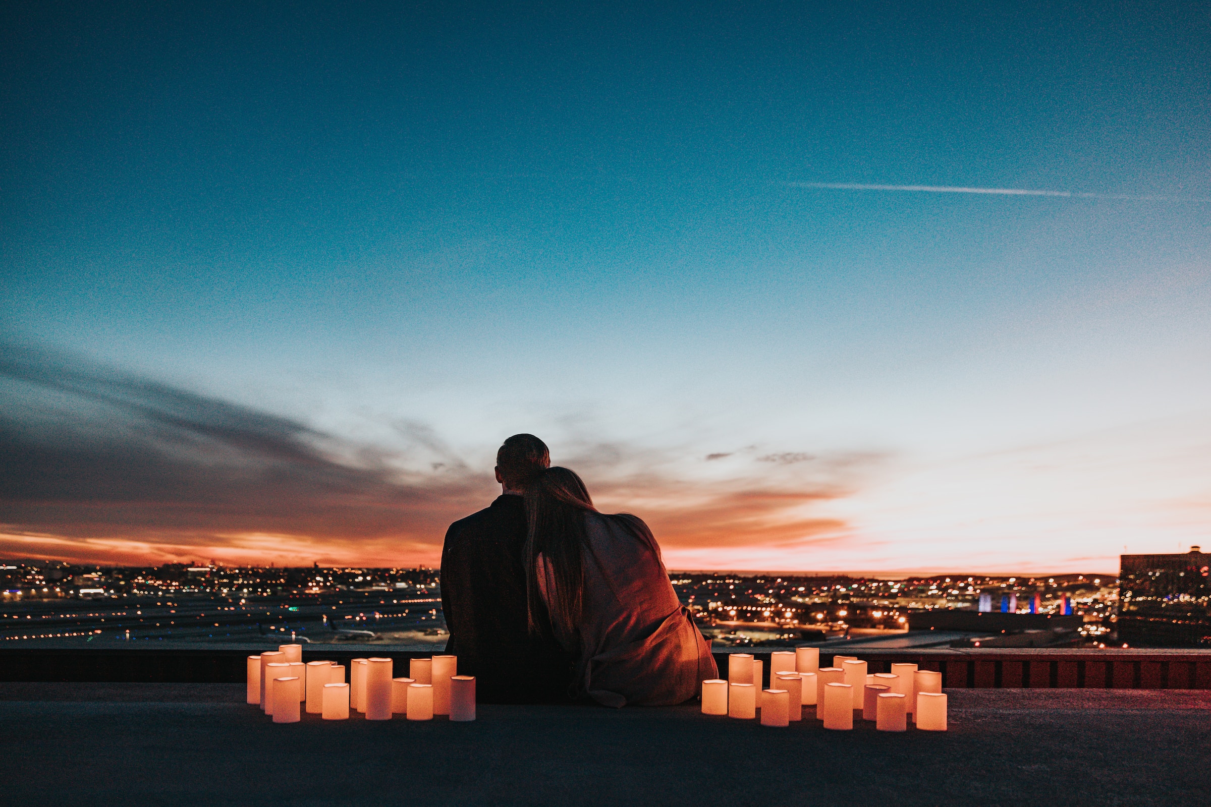 Woman leaning on a man's shoulder, surrounded by candle lights and overling the city. | Source: Unsplash