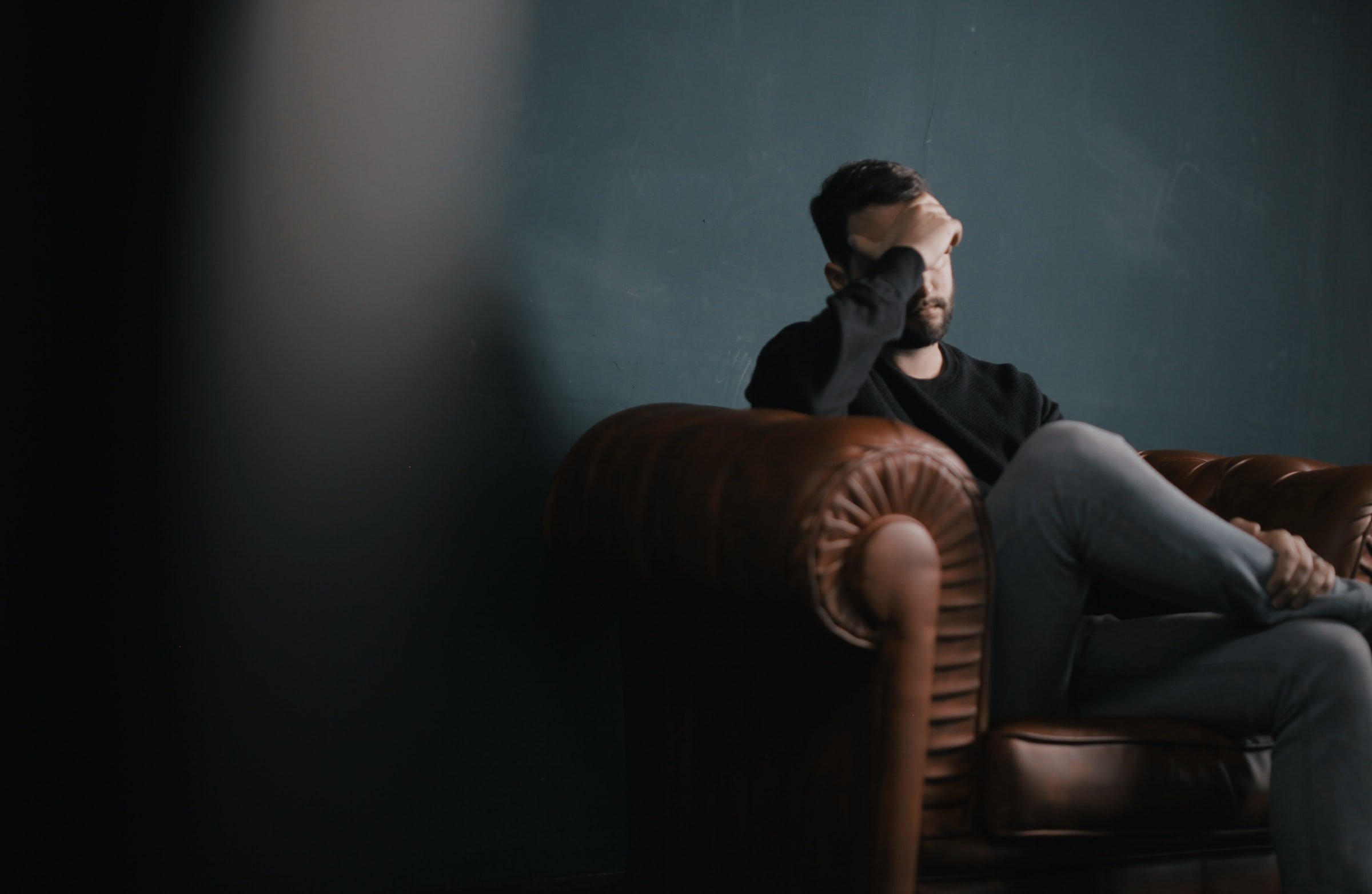 Man sitting on a couch with a hand on his face. | Source: Unsplash