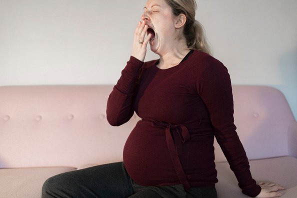 Young pregnant woman pictured sitting on a sofa yawning with tiredness | Photo: Getty Images