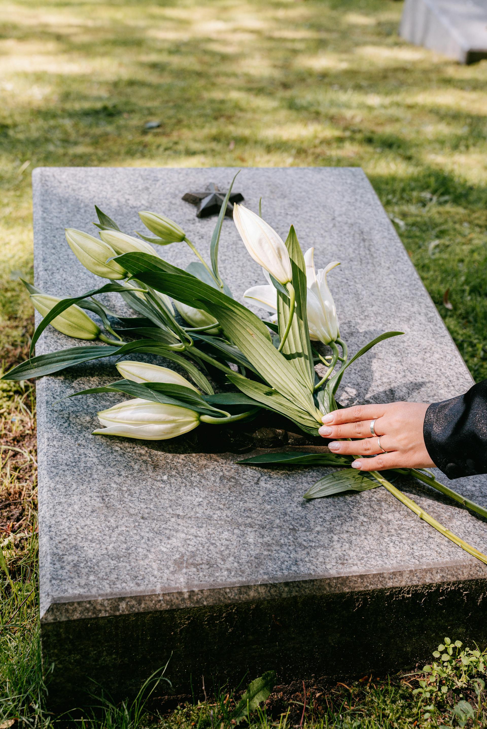 A closeup shot of a woman laying flowers on a tombstone | Source: Pexels