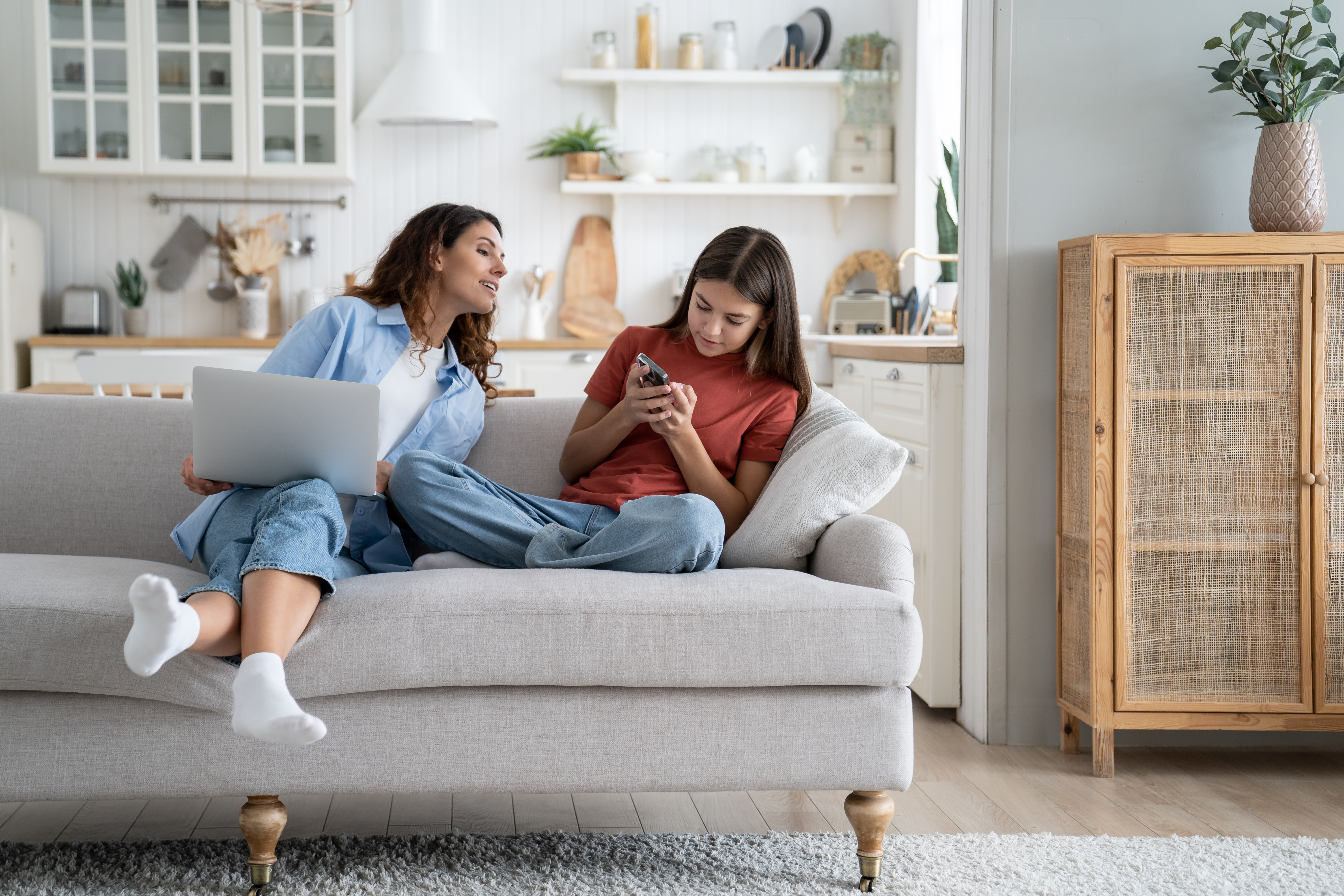 Independent everyday teen girl sits on sofa keeps secrets from mom woman by hiding phone screen | Source: Getty Images