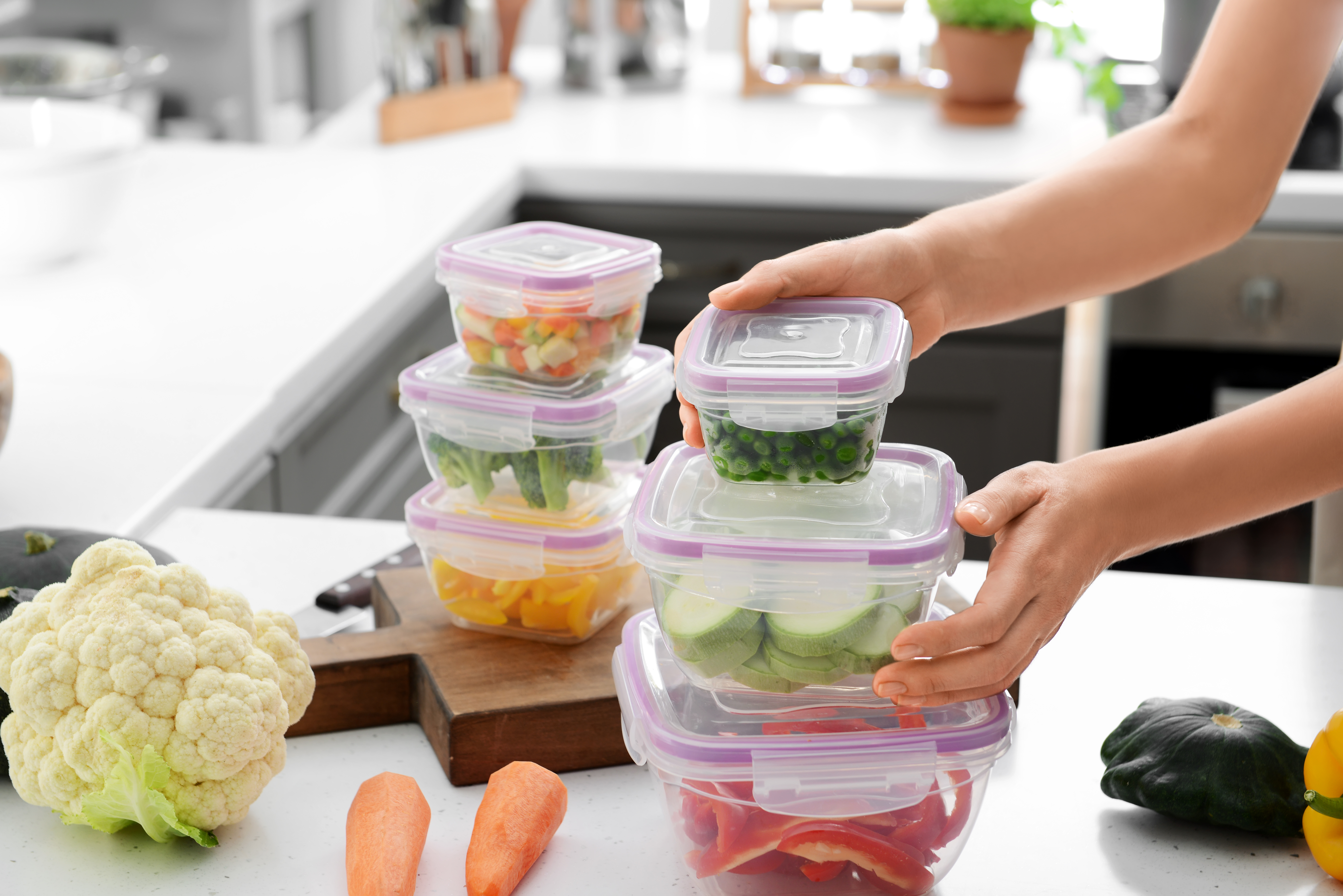 Woman holding stack of plastic containers with fresh vegetables for freezing at table in kitchen | Source: Shutterstock