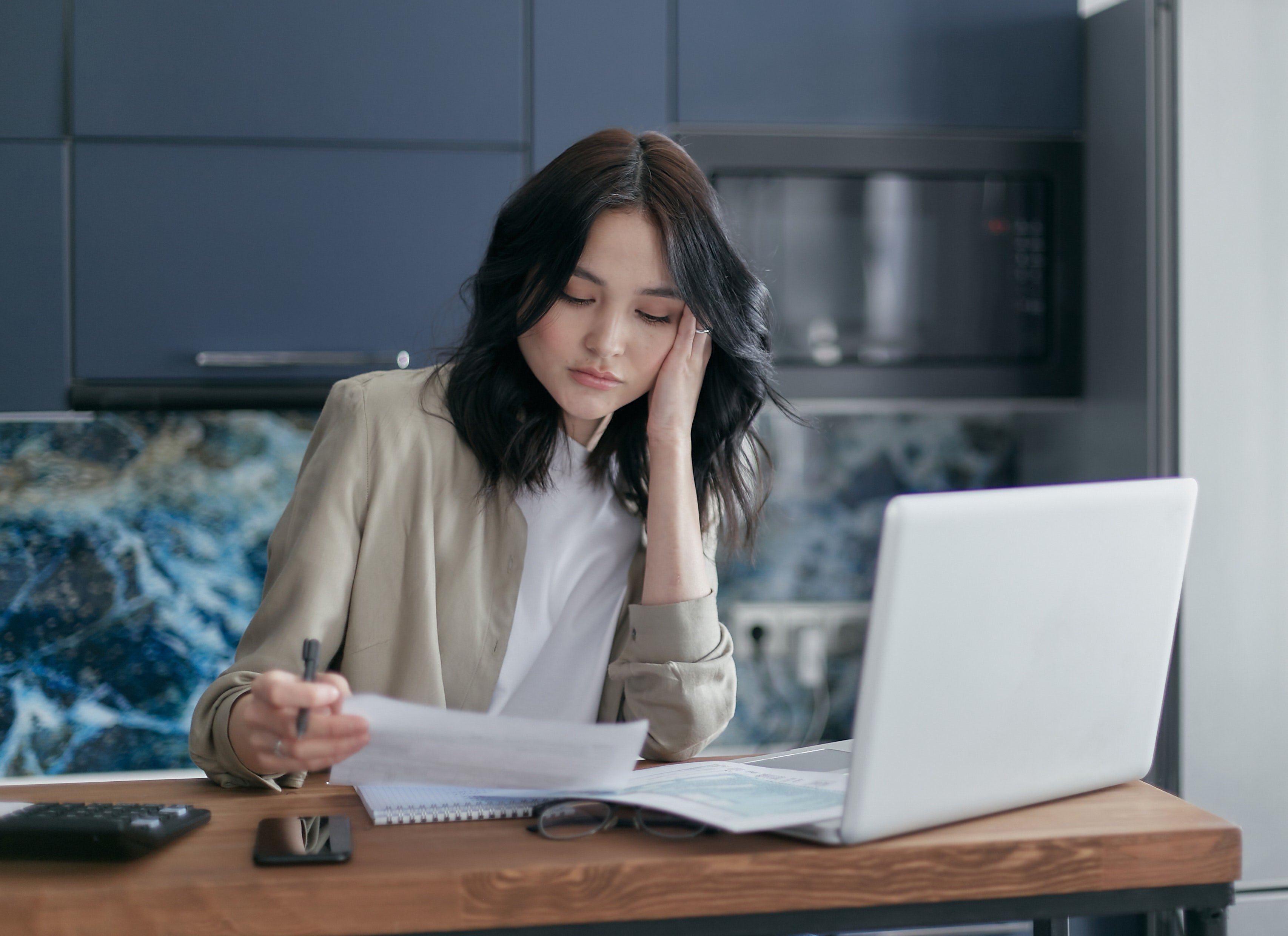 A woman starring down at a document while seated in the kitchen | Source: Pexels