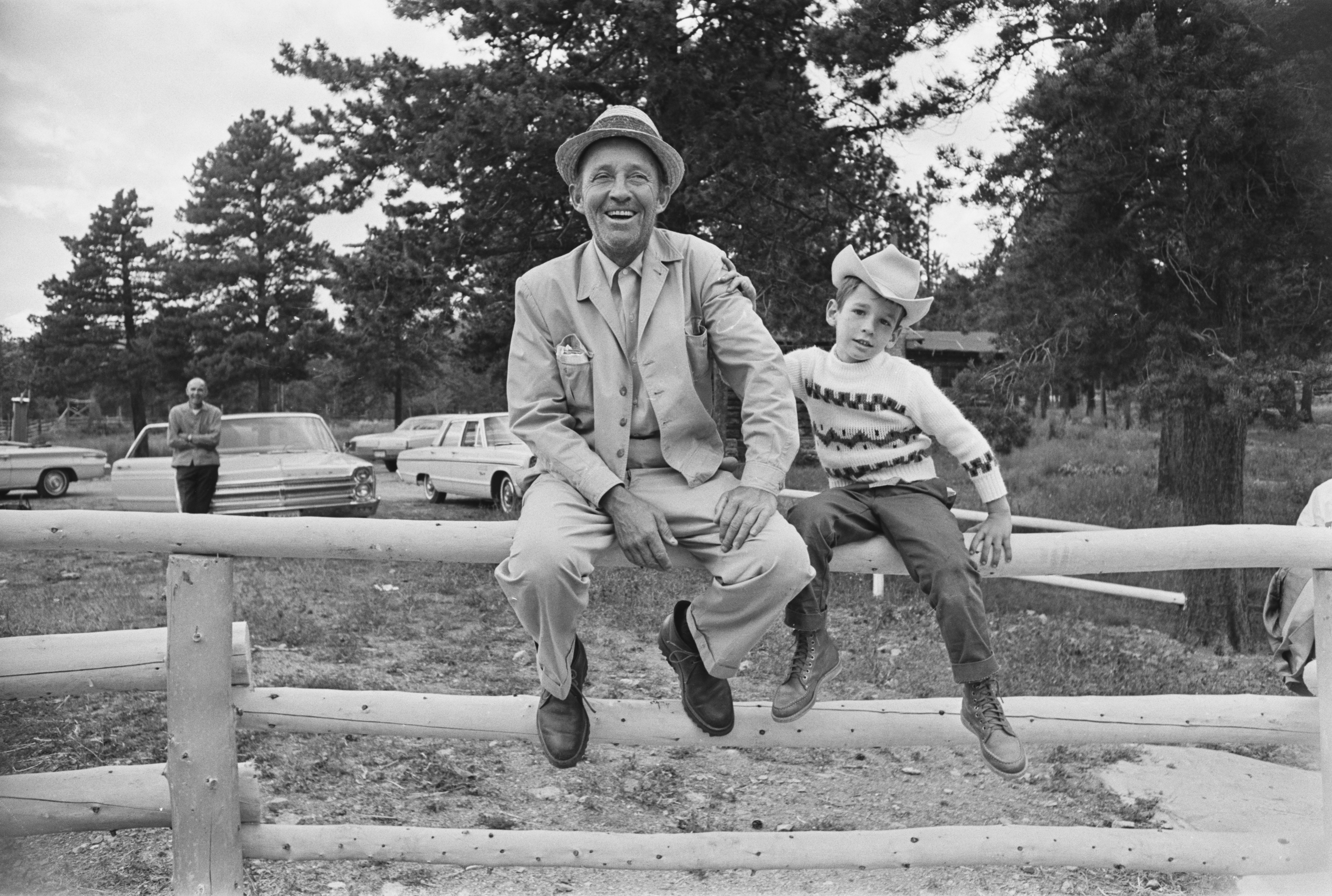 American singer and actor Bing Crosby (1903-1977) with his son Harry Crosby, wearing hats and smiling as they sit on a wooden fence, 1965. | Source: Getty Images