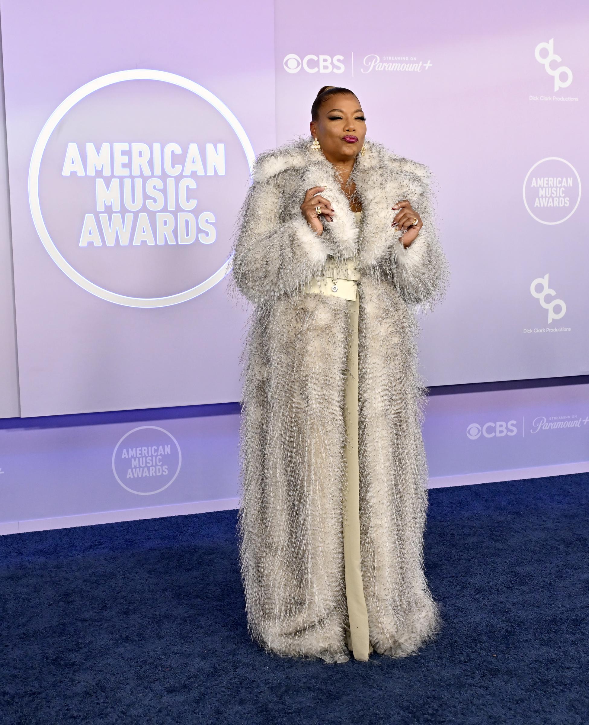 Queen Latifah puckers her lips and raises both hands near her face while posing against a lavender backdrop featuring CBS and Paramount+ branding.