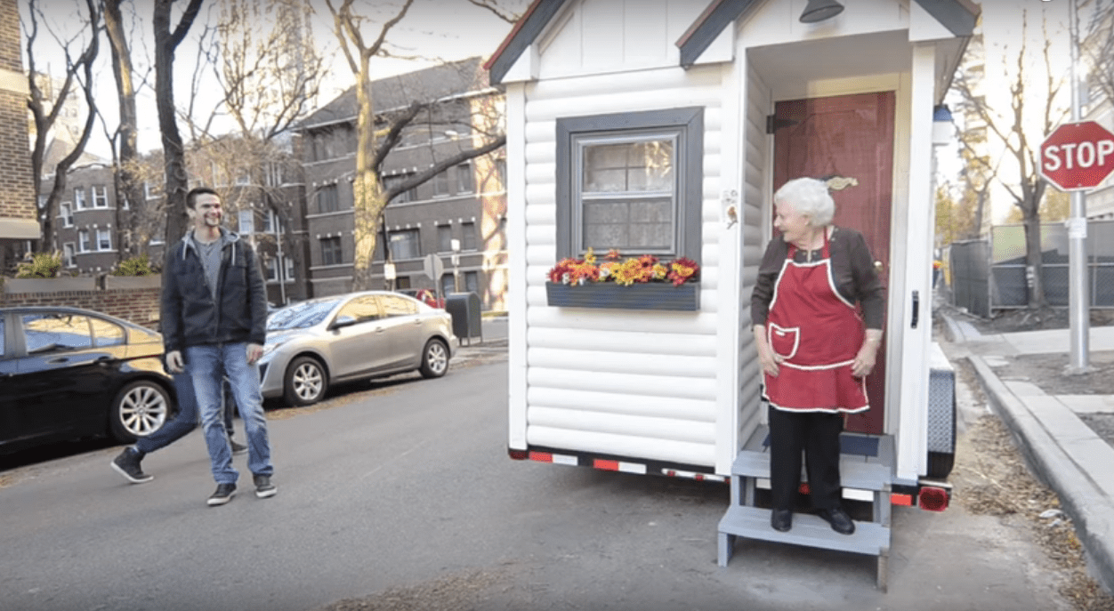 Une "Sausage Nonna" photographiée dans son tablier devant sa petite maison parlant à un jeune homme. | YouTube/officiel Johnsonville