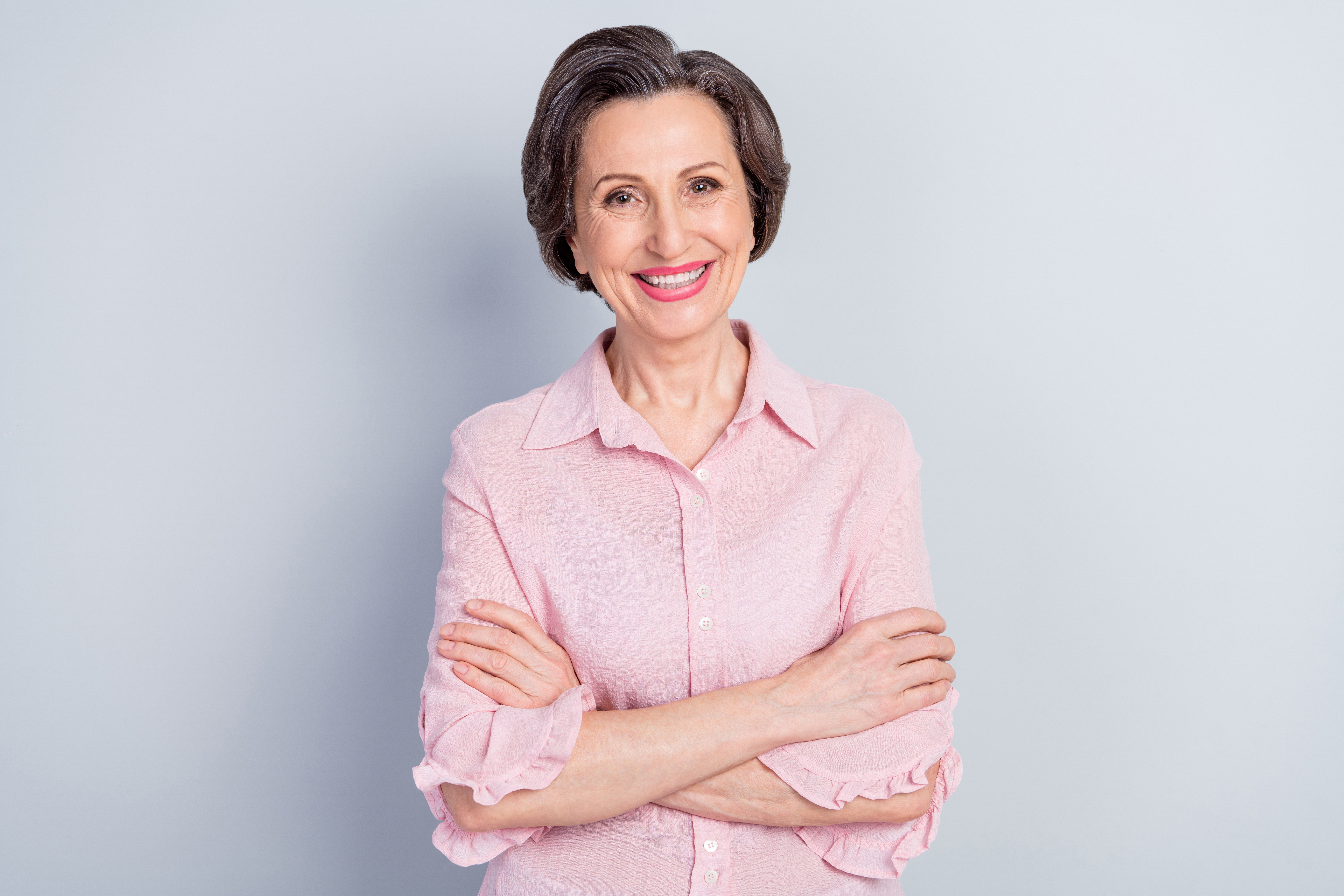 A smiling senior woman standing with her arms crossed | Source: Shutterstock