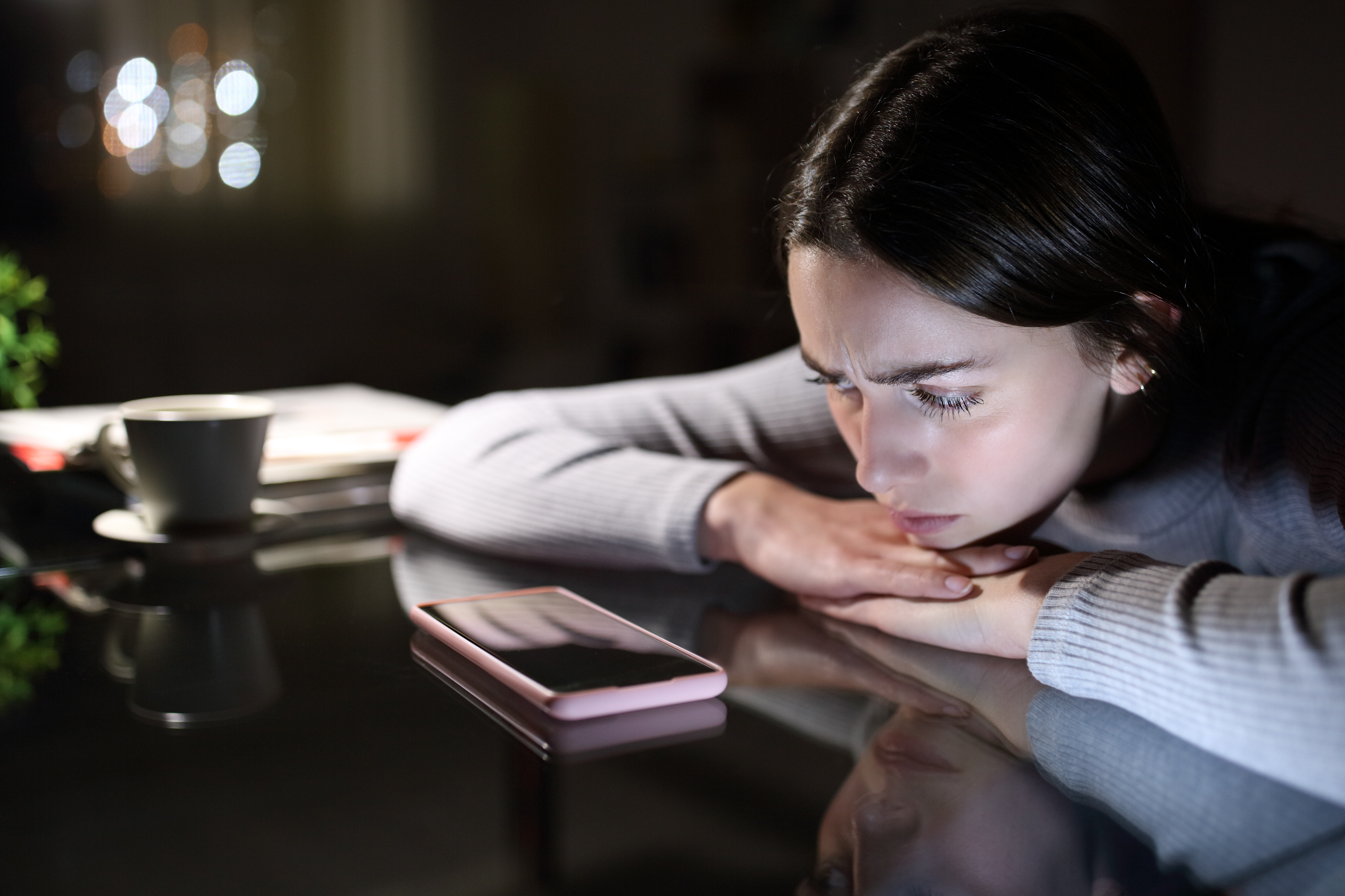 Sad woman with a mobile phone in the night at home. | Source: Shutterstock