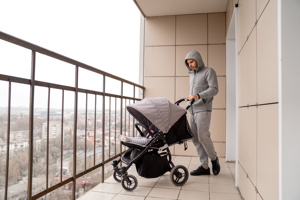 Hombre con un cochecito de bebé asomado en un balcón. | Foto: Shutterstock