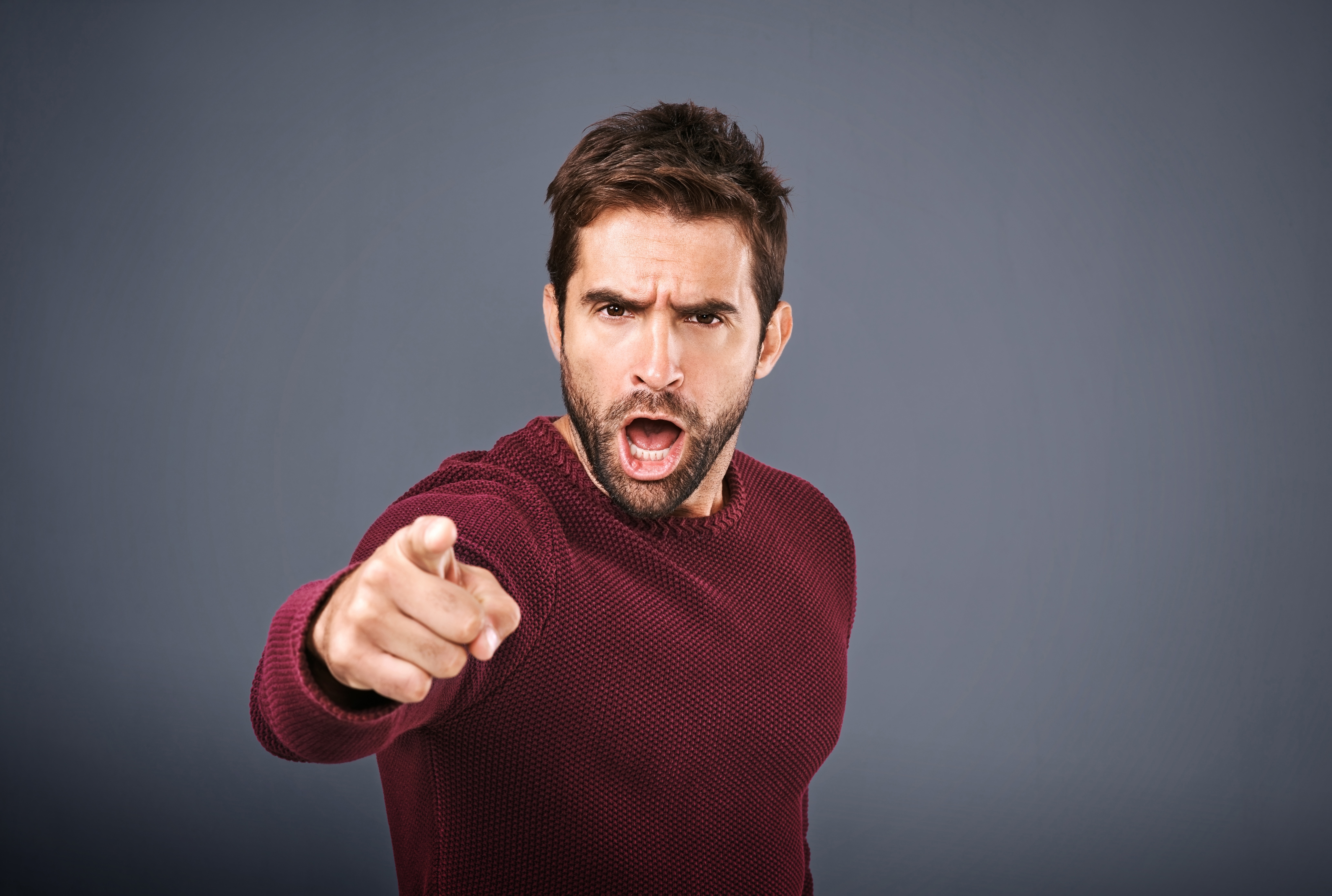 Shot of a man pointing a finger in anger against a gray background. | Source: Shutterstock