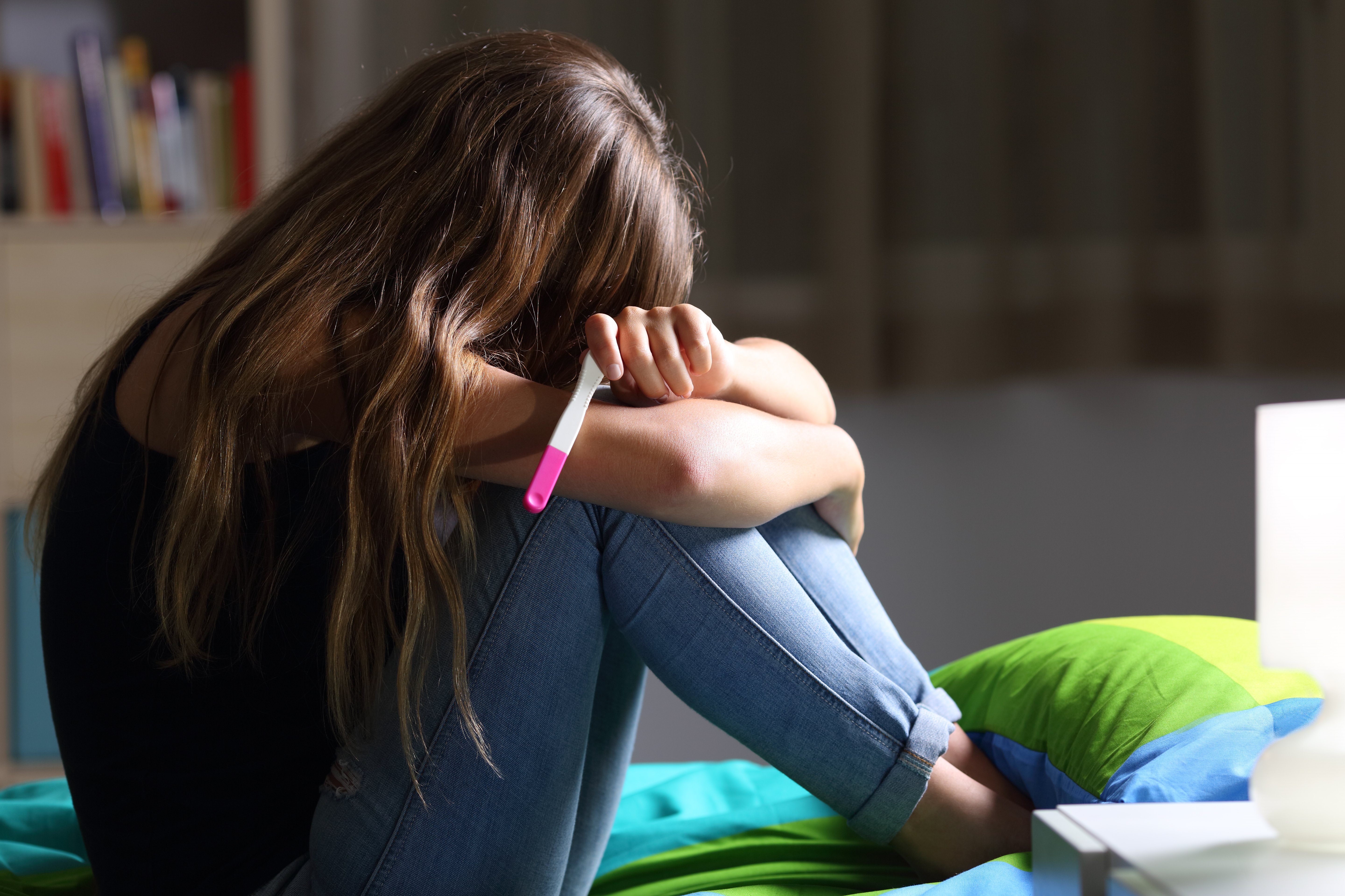 Side view of a sad pregnant teen sitting on her bed after checking a pregnancy test | Photo: Shutterstock.com