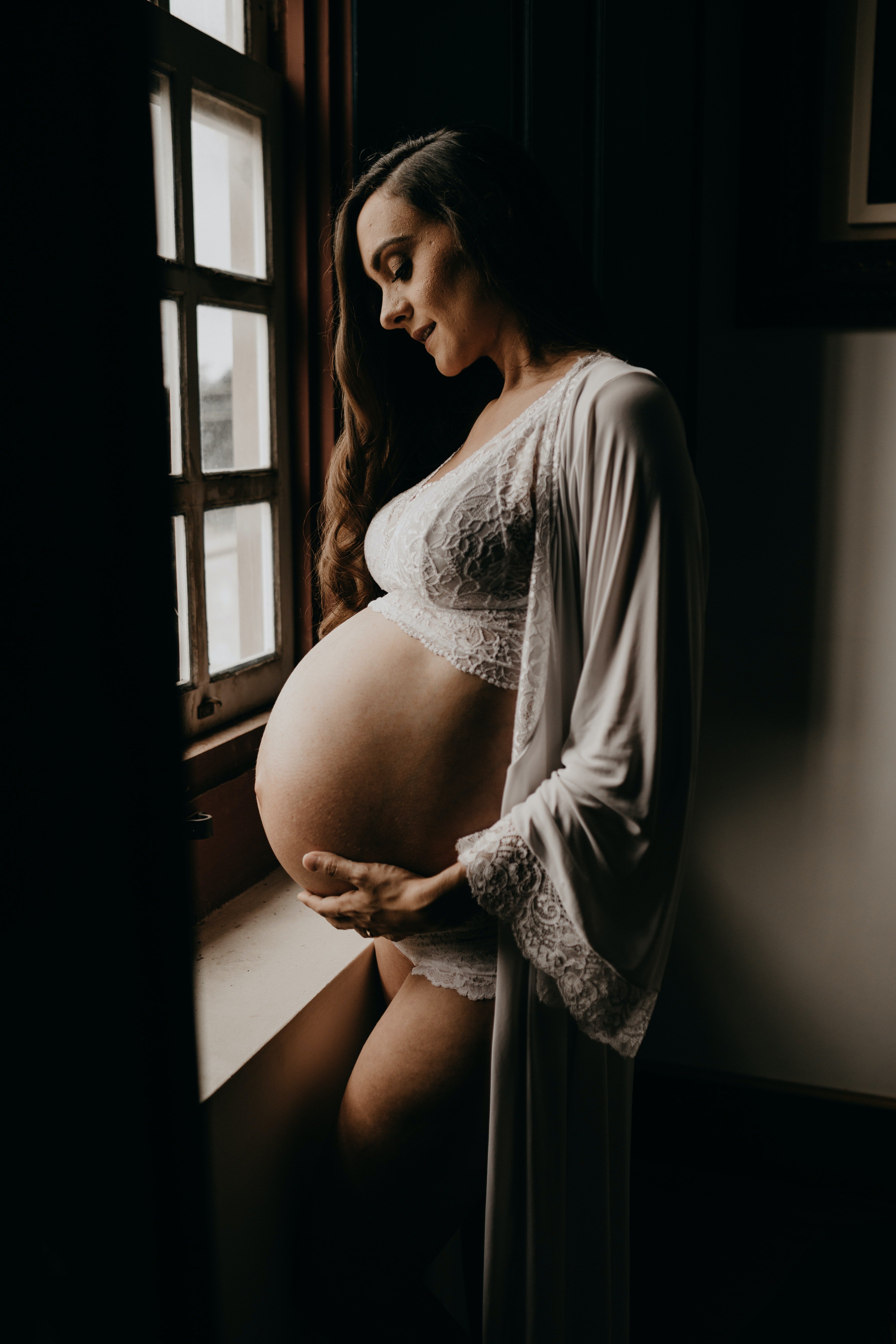 Schwangere Frau, die neben dem Fenster eine Strickjacke trägt. | Quelle: Pexels