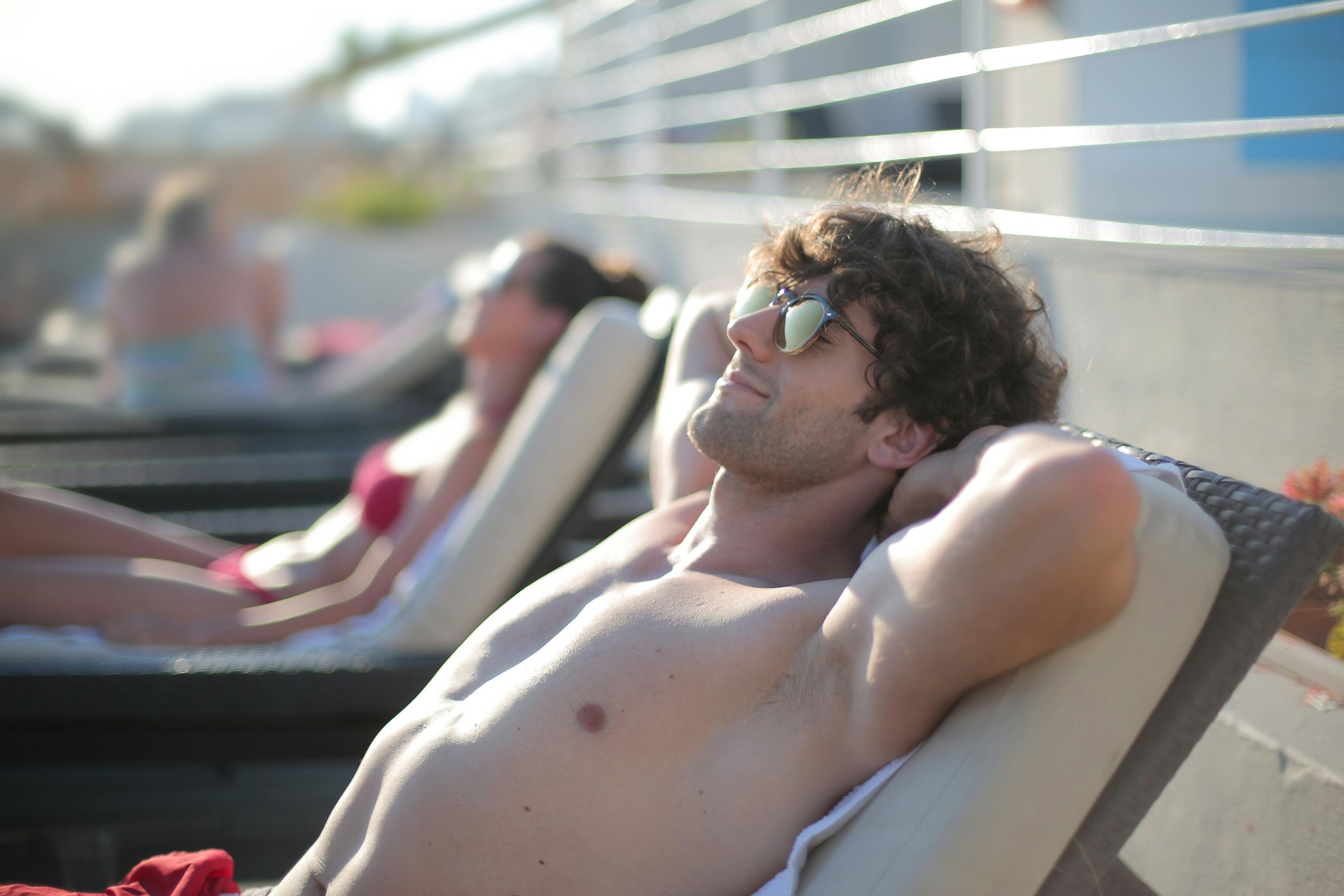A happy man wearing sunglasses while lying on a sunbed | Source: Pexels