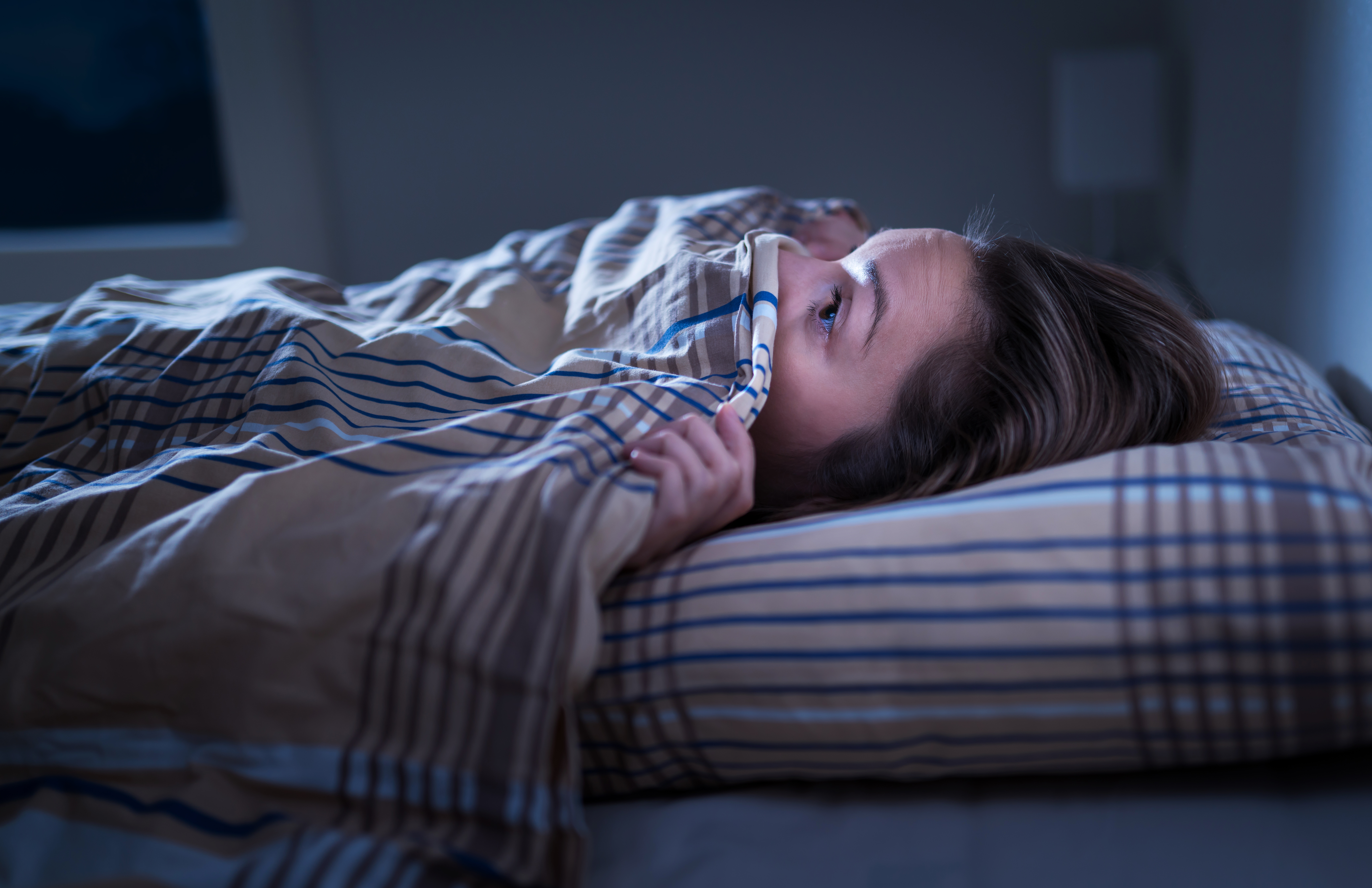 Scared woman hiding under blanket. Afraid of the dark. Unable to sleep after nightmare or bad dream. Awake in the middle of the night in bedroom at home. Monster under the bed. | Source: Getty Images