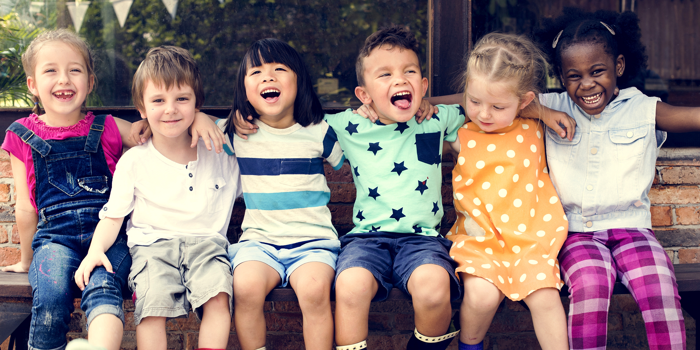 Cheerful little kids sitting on a bench and laughing | Source: Shutterstock