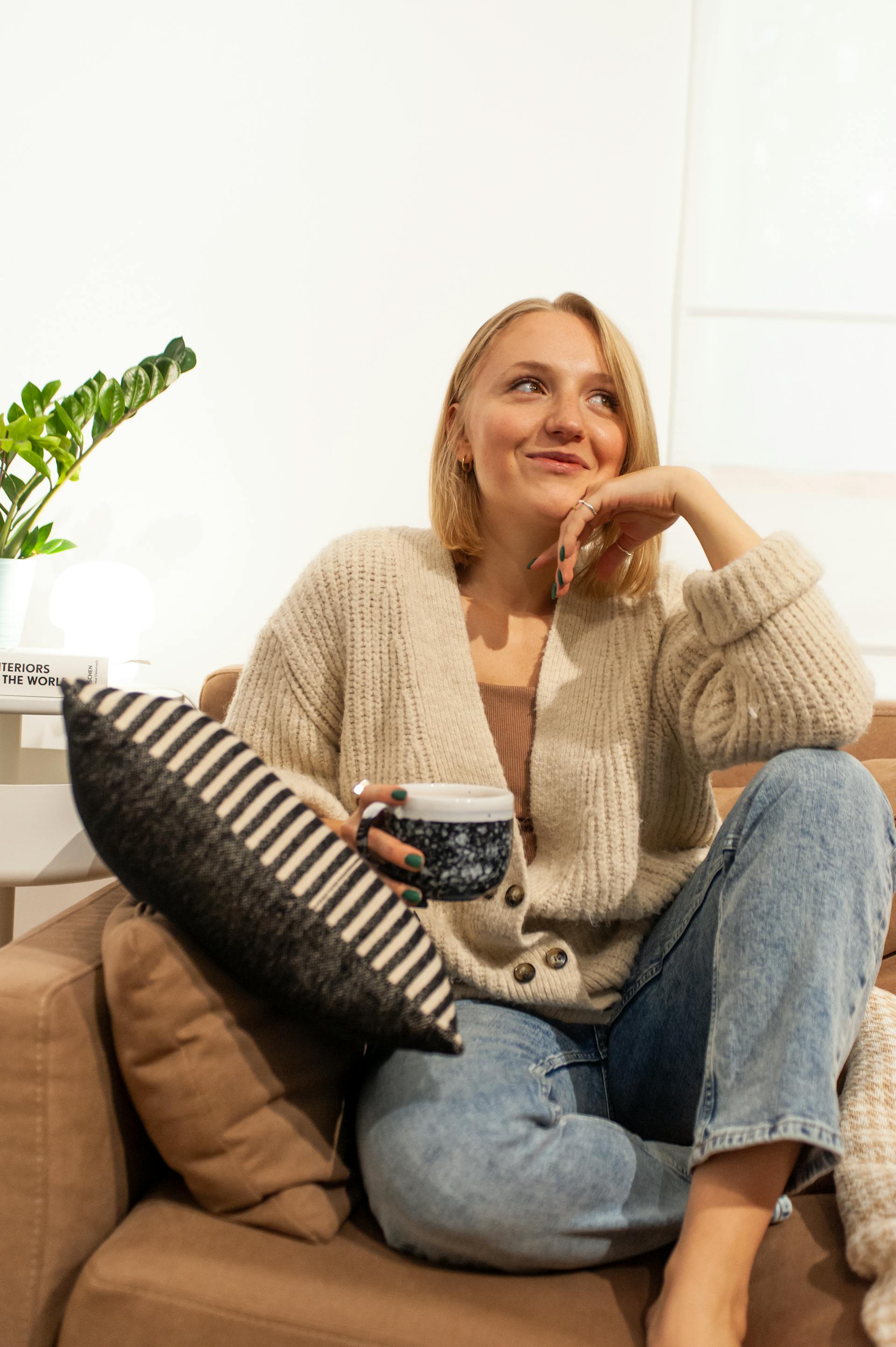 A smiling woman sitting on a sofa while holding a cup of coffee | Source: Pexels