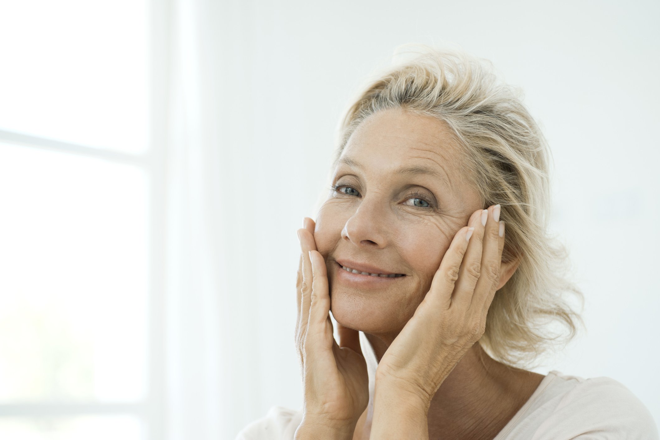 Femme mûre touchant les joues, souriant. | Photo : Getty Images