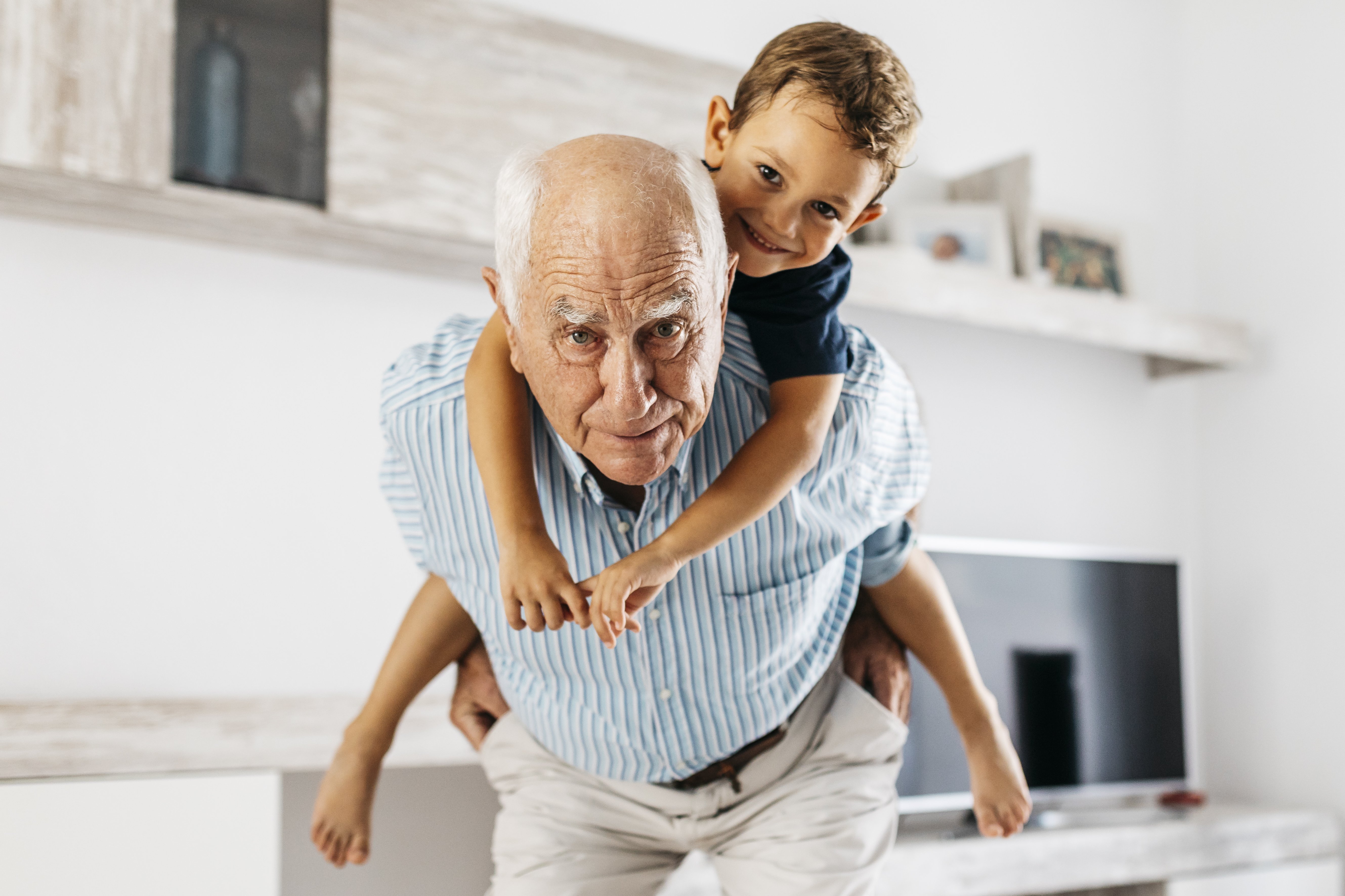 Portrait of grandfather giving his grandson a piggyback ride in the living room | Photo: Getty Images