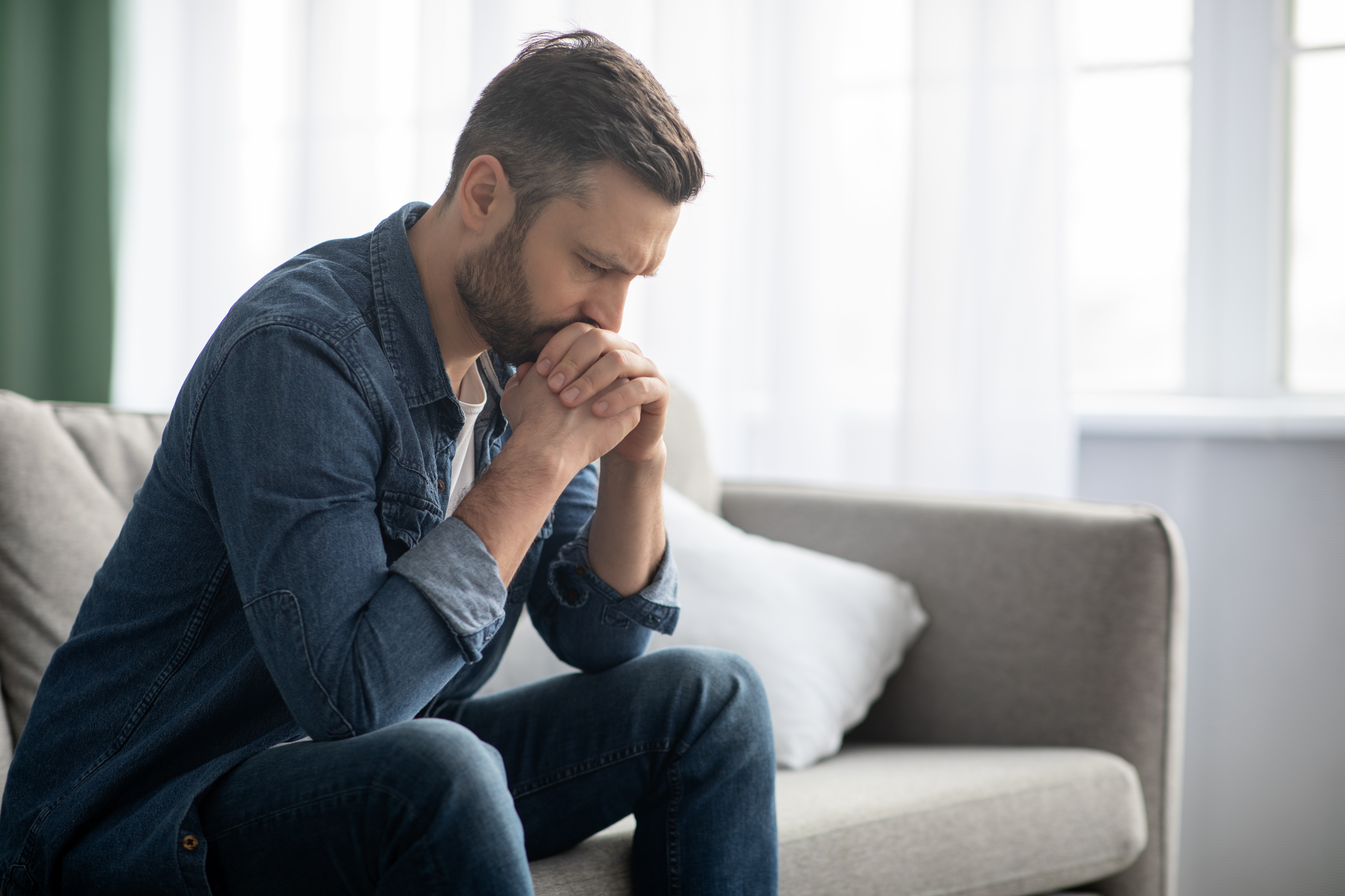 A man looking down while sitting on a couch | Source: Shutterstock