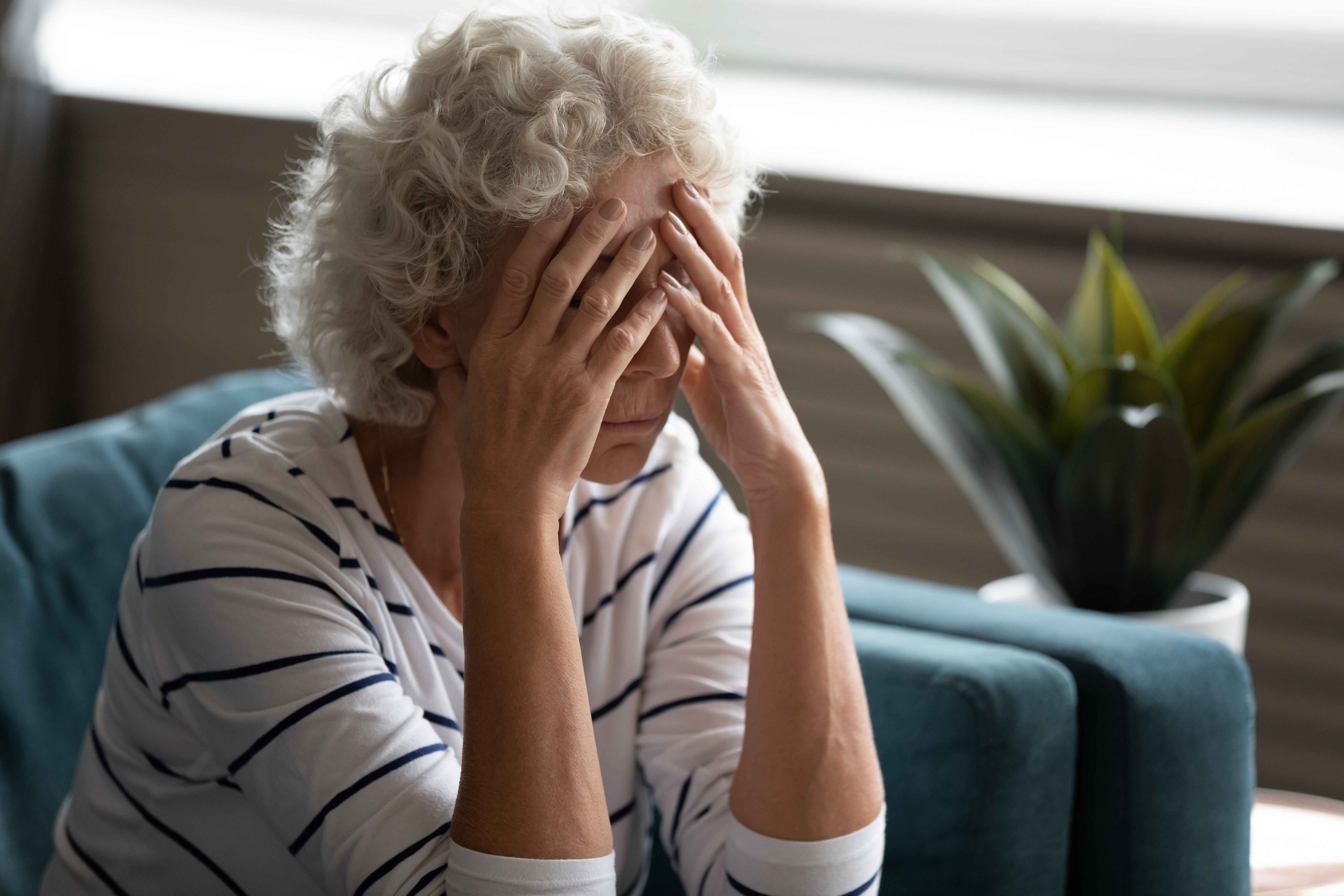 An upset older woman covering her face while seated | Source: Shutterstock