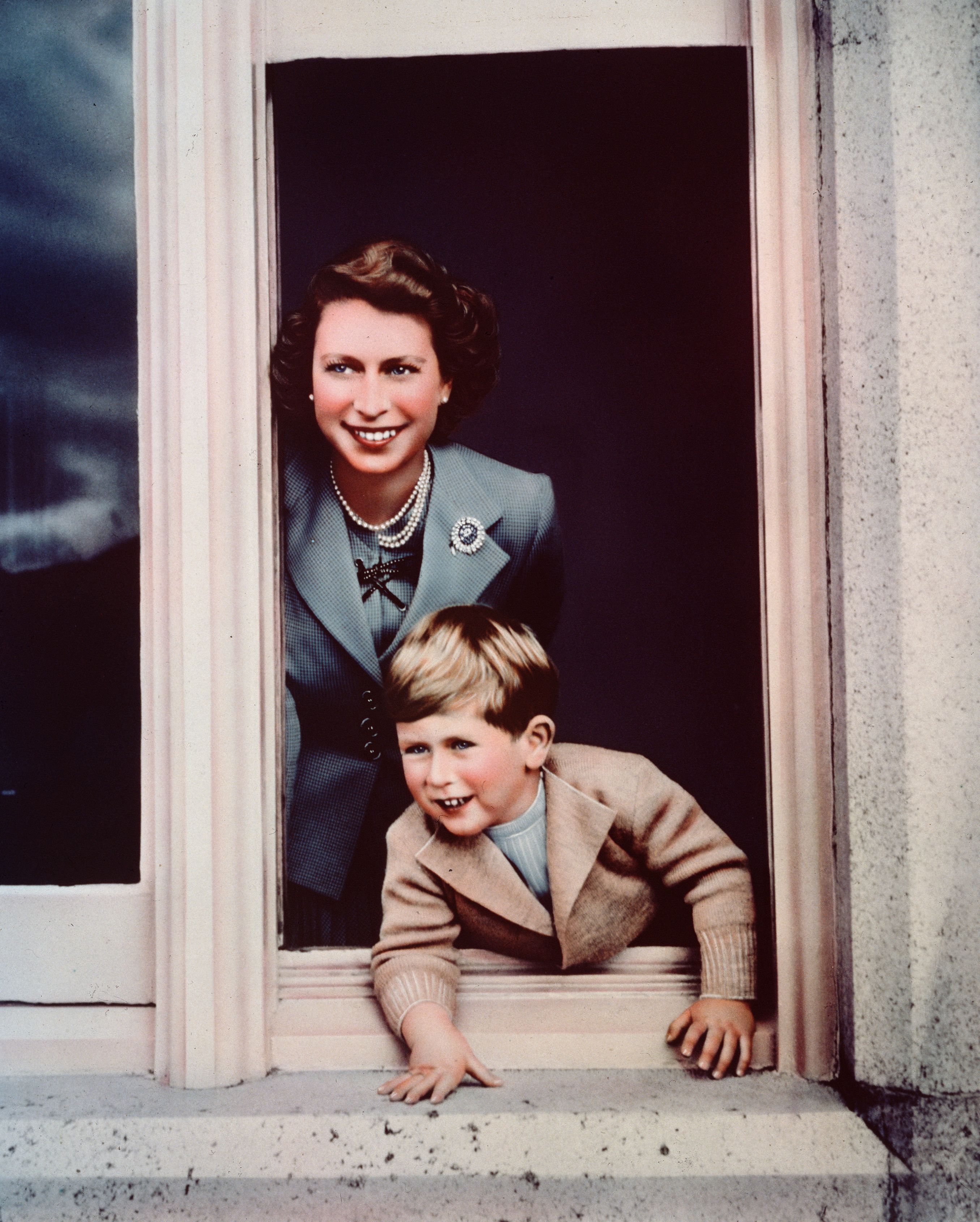 In a charming moment captured in September 1952 at Balmoral, Princess Elizabeth is seen smiling as a young Prince Charles leans eagerly out of a window, the pair sharing a candid and playful exchange that reflects their close bond just months before her coronation.