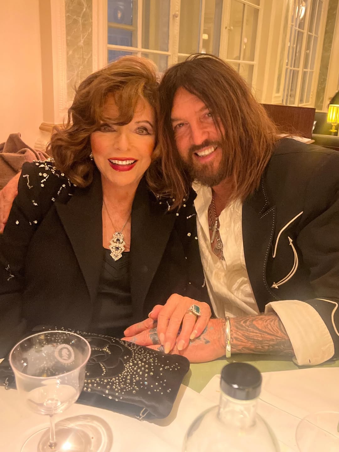 Dame Joan Collins and Billy Ray Cyrus pose for a photo on 15 April 2026. | Source: Instagram/joancollinsdbe