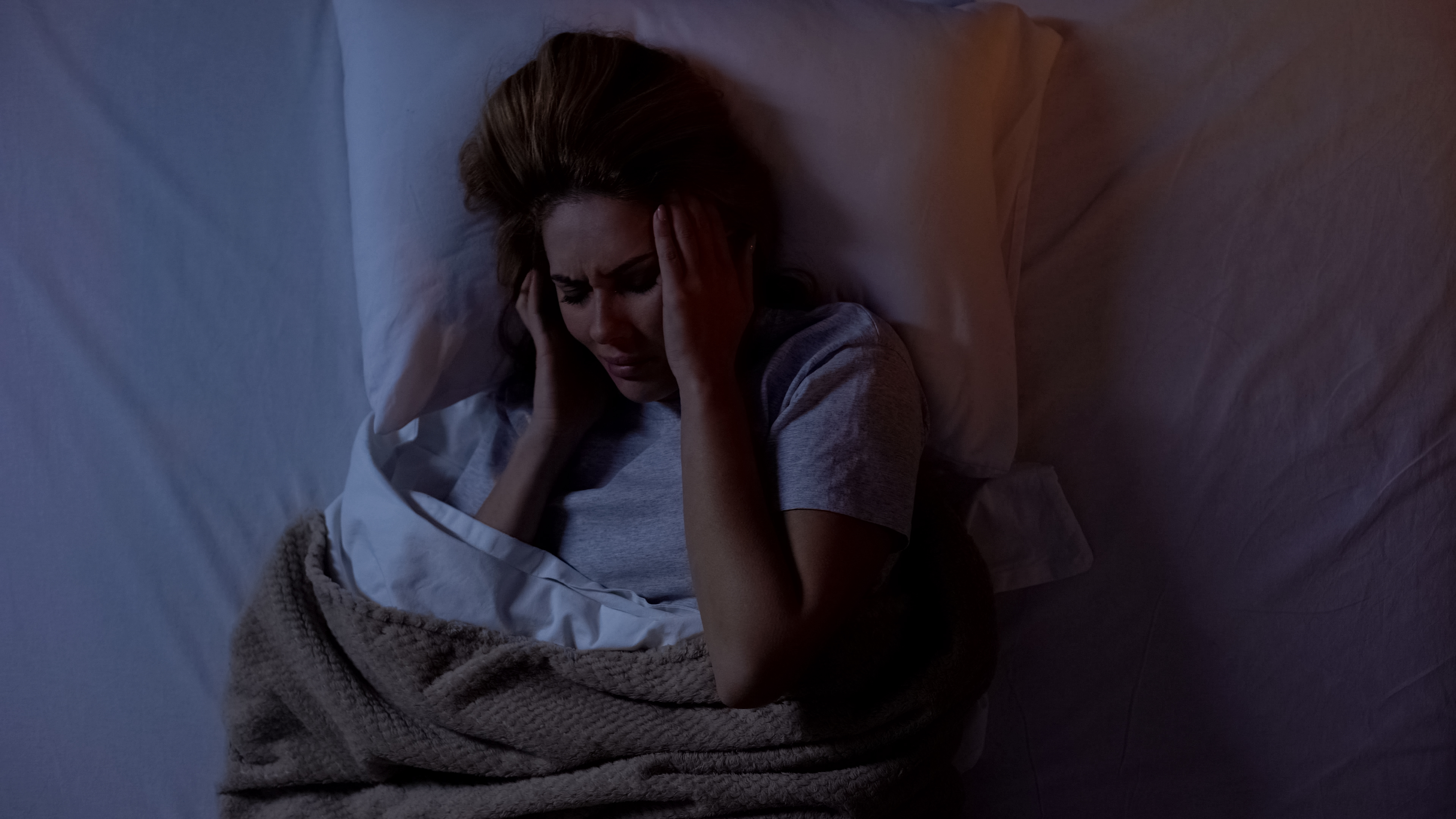 Lady holding head in bed, suffering headache after awakening at night. | Source: Shutterstock