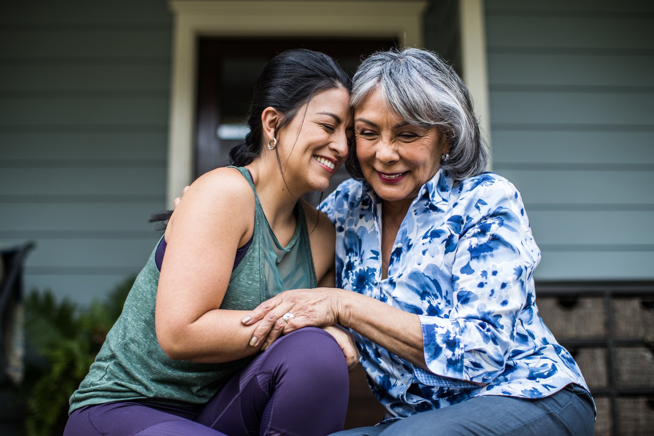 An older woman and her adult daughter laughing and hugging each other on the porch. | Source: Getty Images