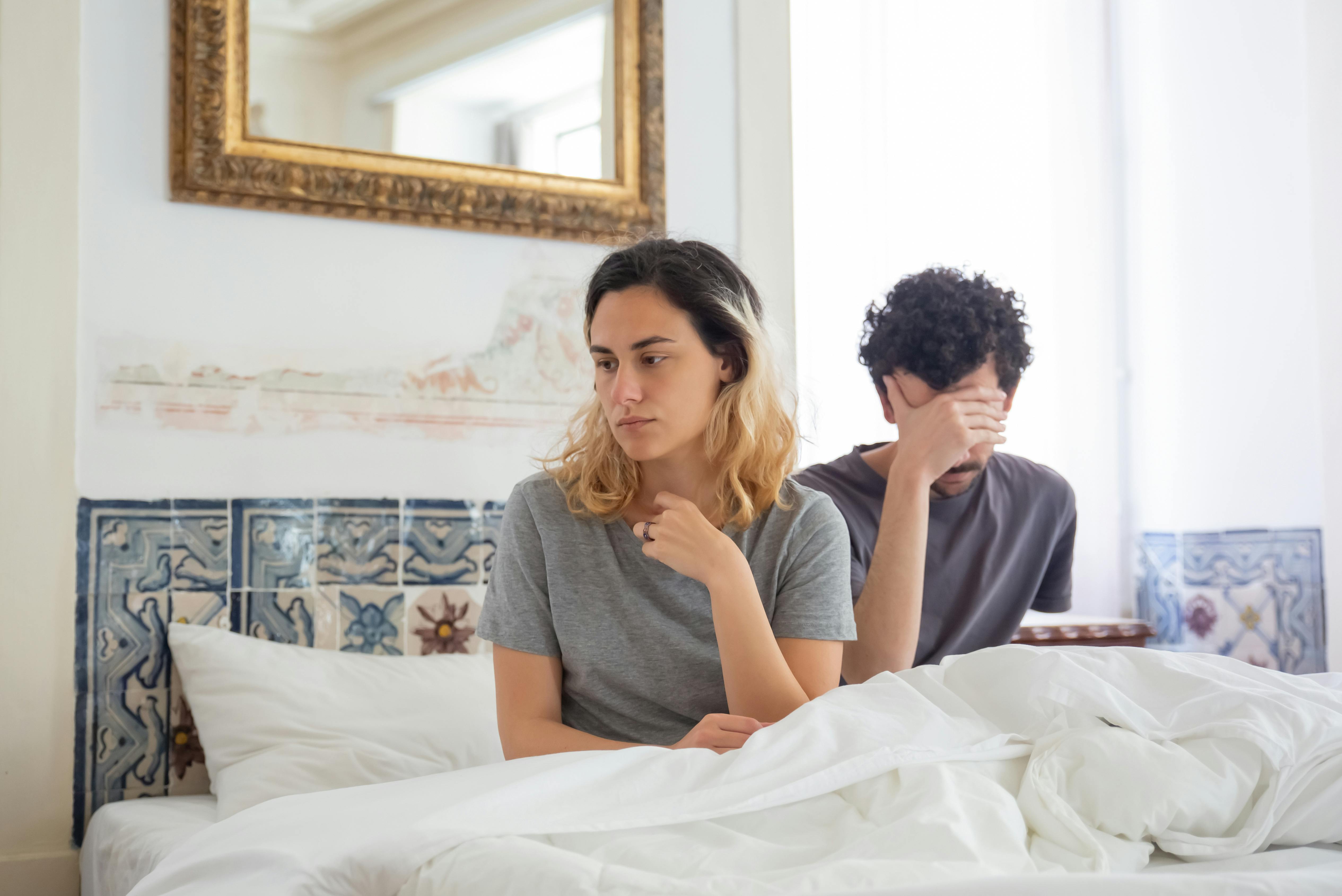 A dismayed-looking couple sitting up in bed | Source: Pexels