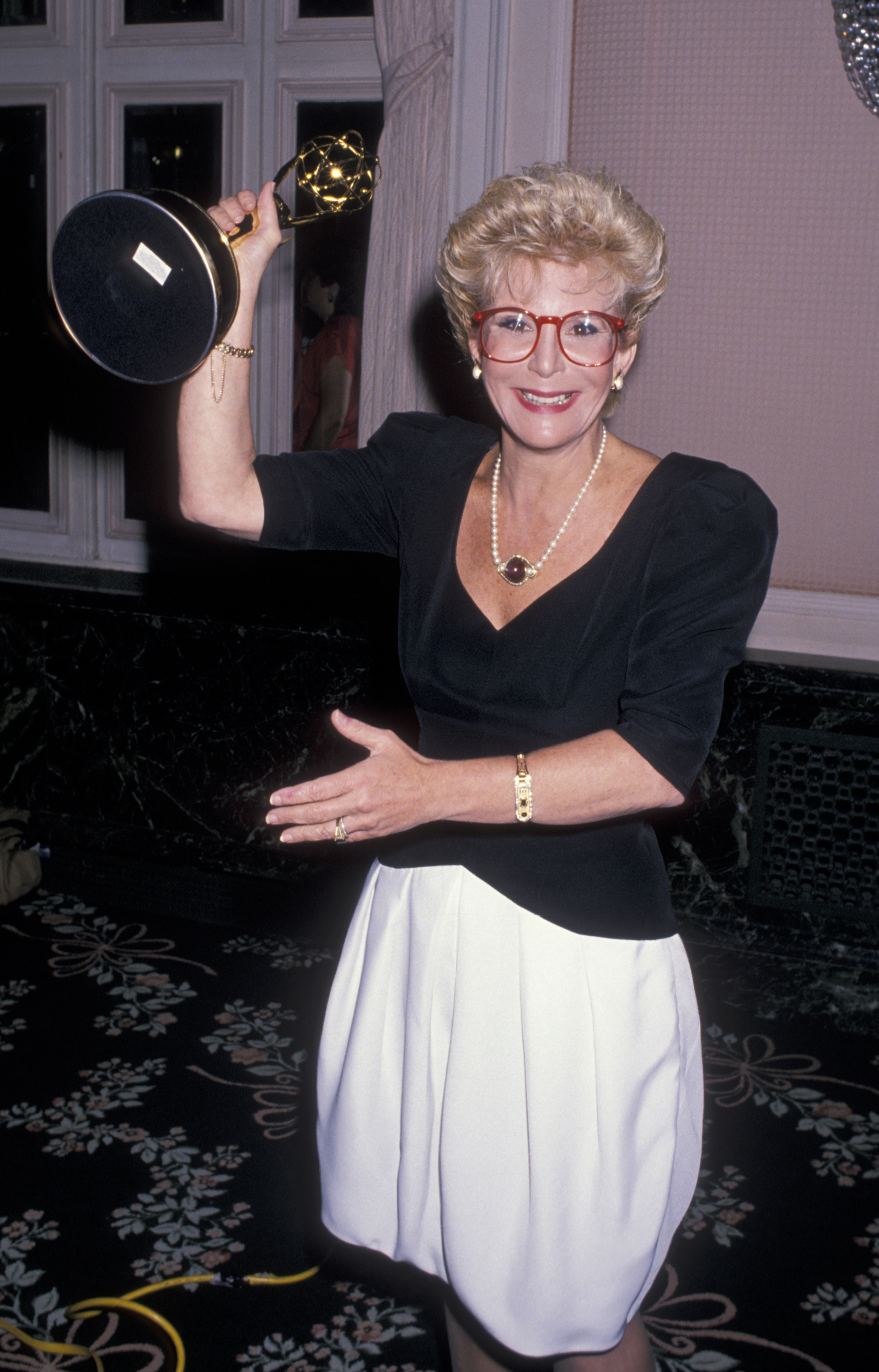 Sally Jessy Raphael beams with pride while holding up her Emmy at the 16th Annual Daytime Emmy Awards, held at the Waldorf Hotel in New York City on June 29, 1989. Her signature red glasses and black-and-white ensemble complete the celebratory look.