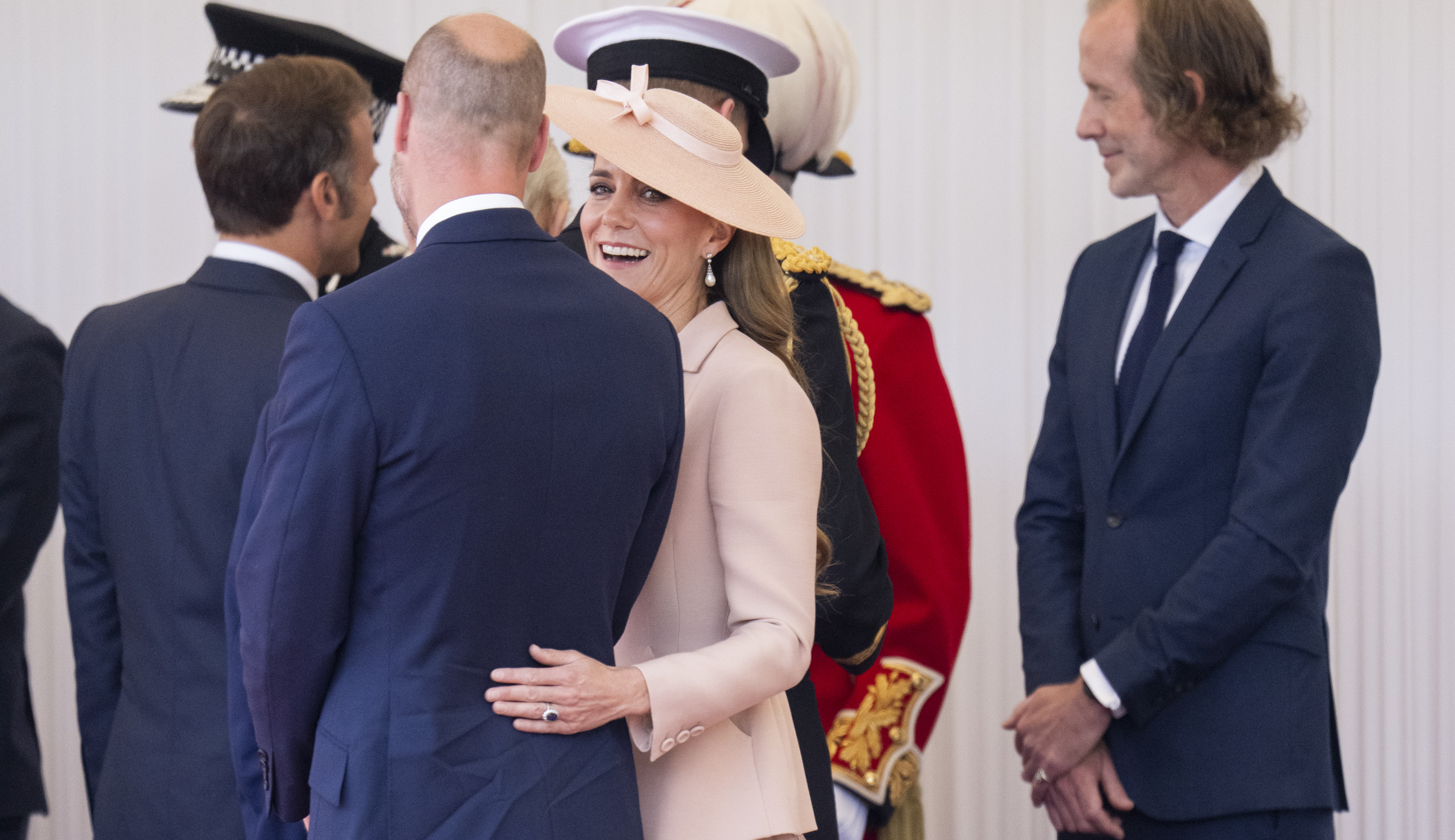 Princess Catherine looks at the camera as she lovingly places her hand on Prince William's back.