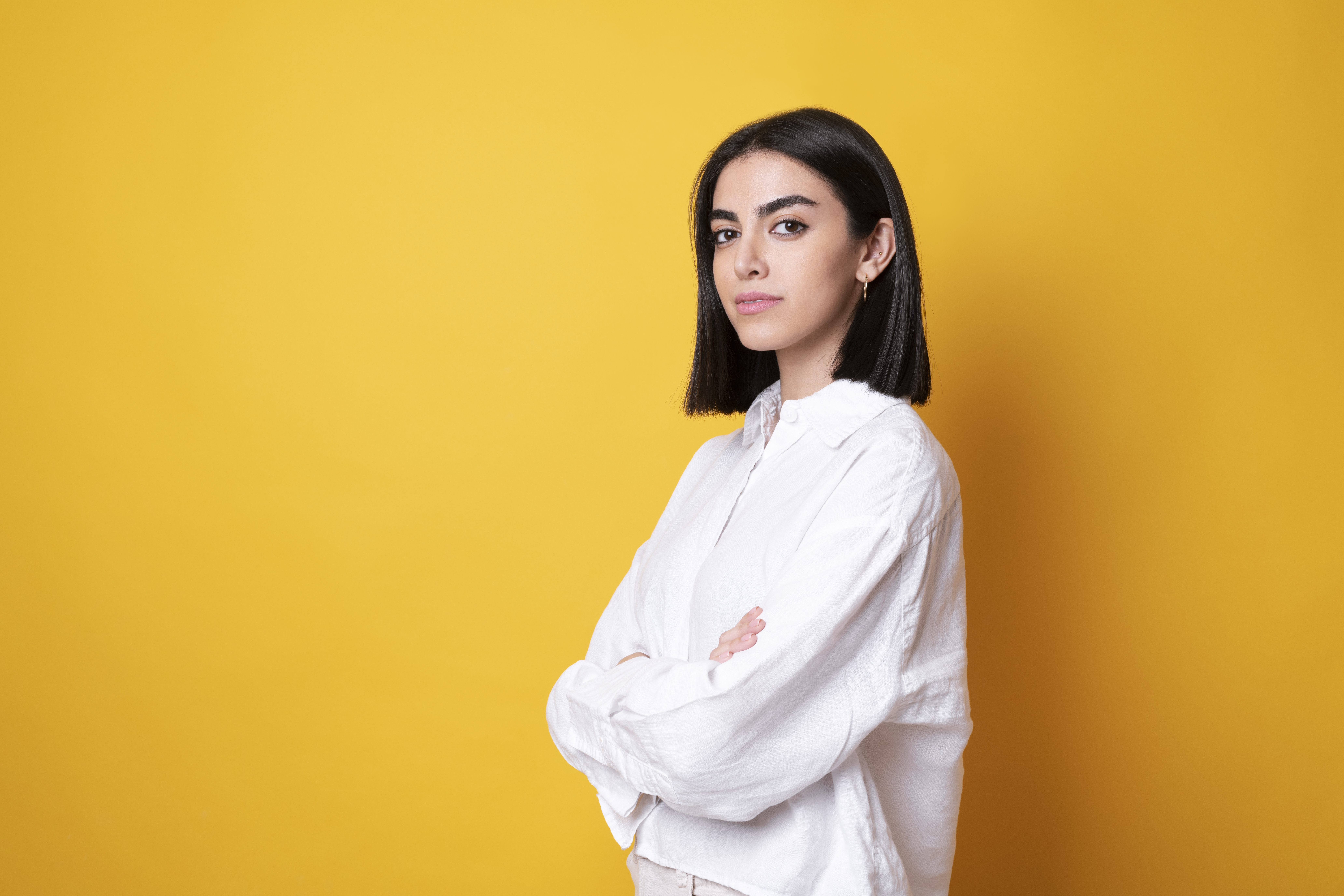 Young woman standing with arms crossed against yellow background | Source: Getty Images