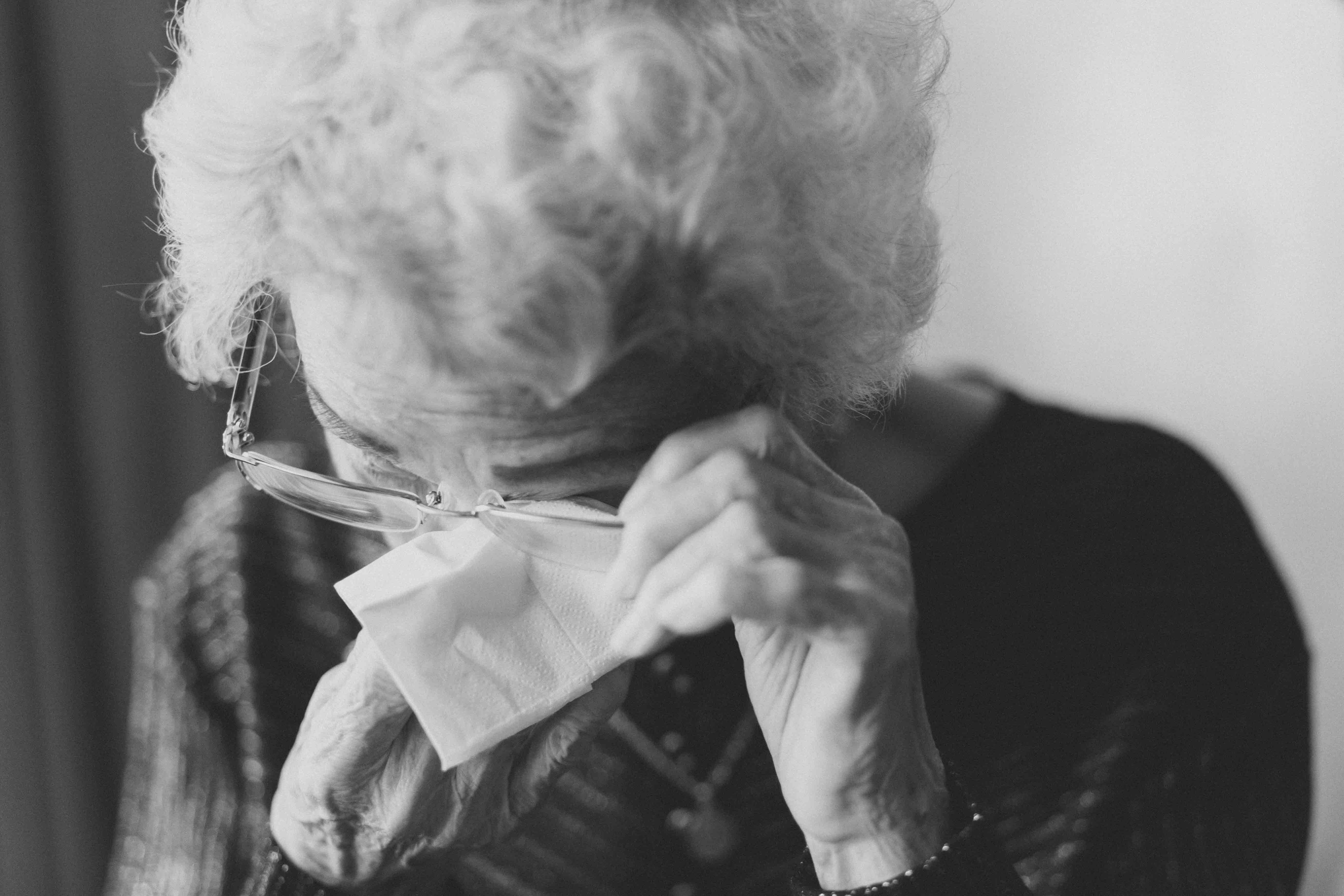 An older woman lifts her glasses and wipes her eyes with a napkin | Source: Unsplash