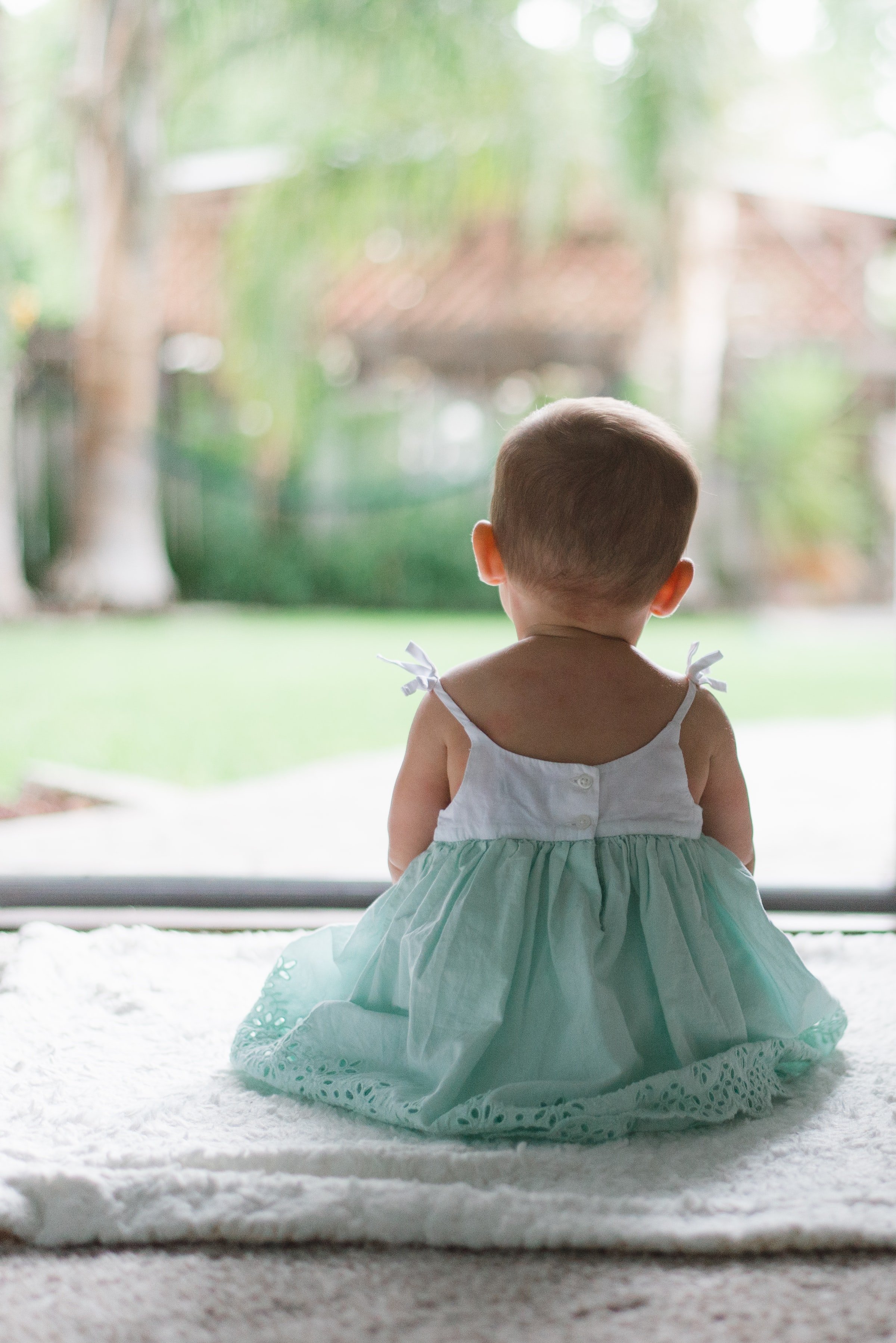 A little girl dressed in a green and white frock is pictured sitting outside. | Source: Unsplash