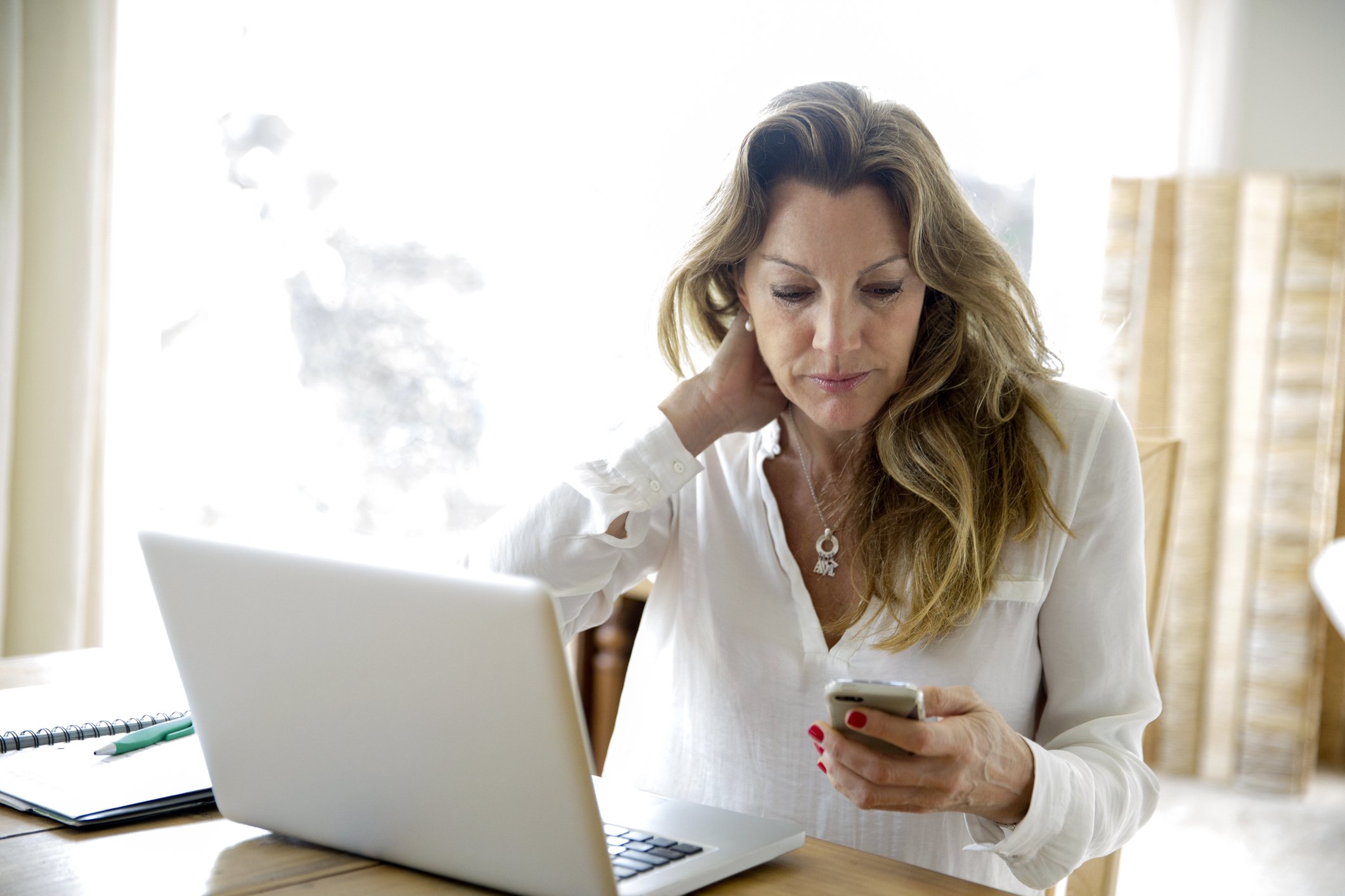 Frau mit Laptop beim Lesen von Smartphone-Text zu Hause | Quelle: Getty Images