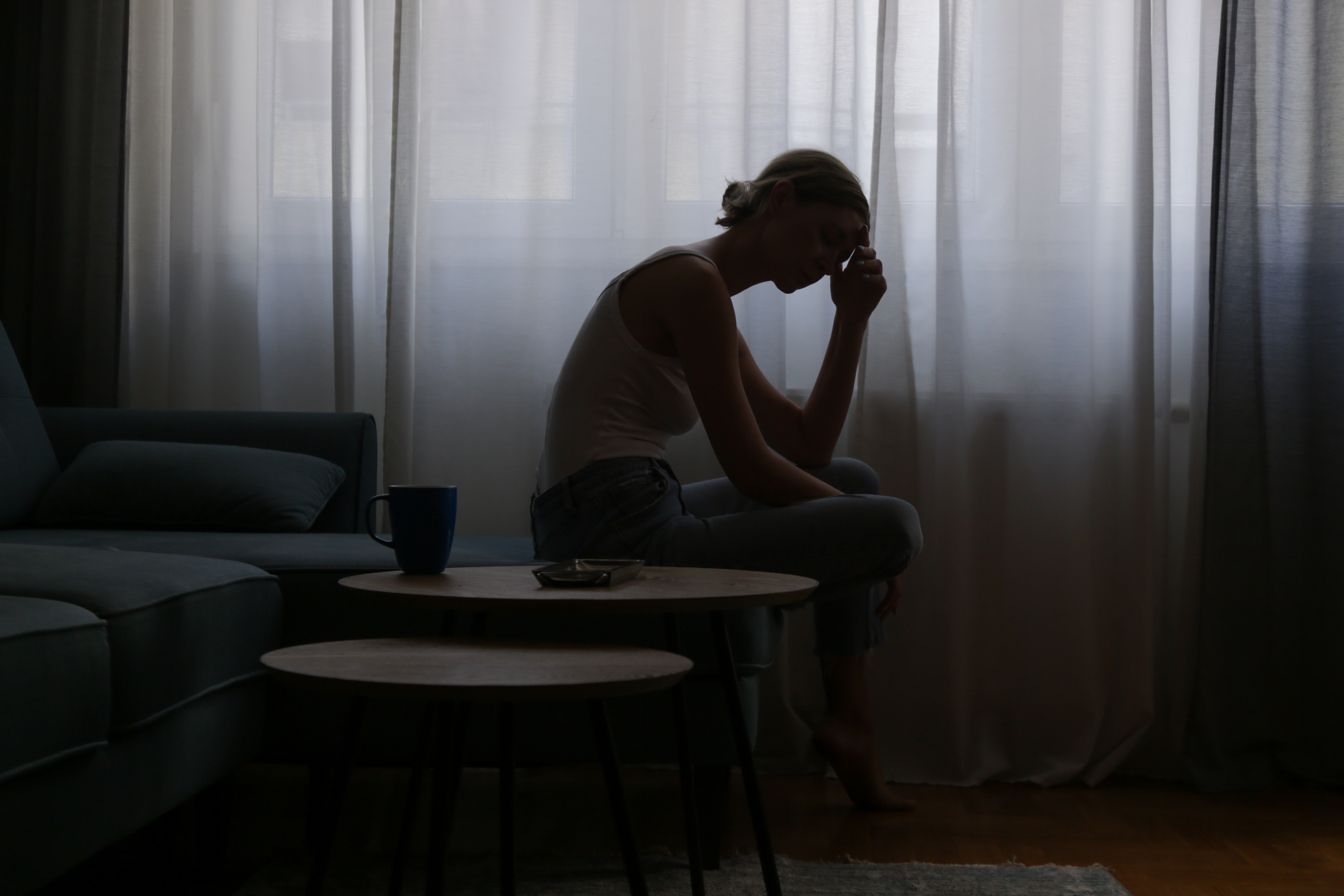 Depressed young woman sitting on a sofa next to a window | Source: Shutterstock
