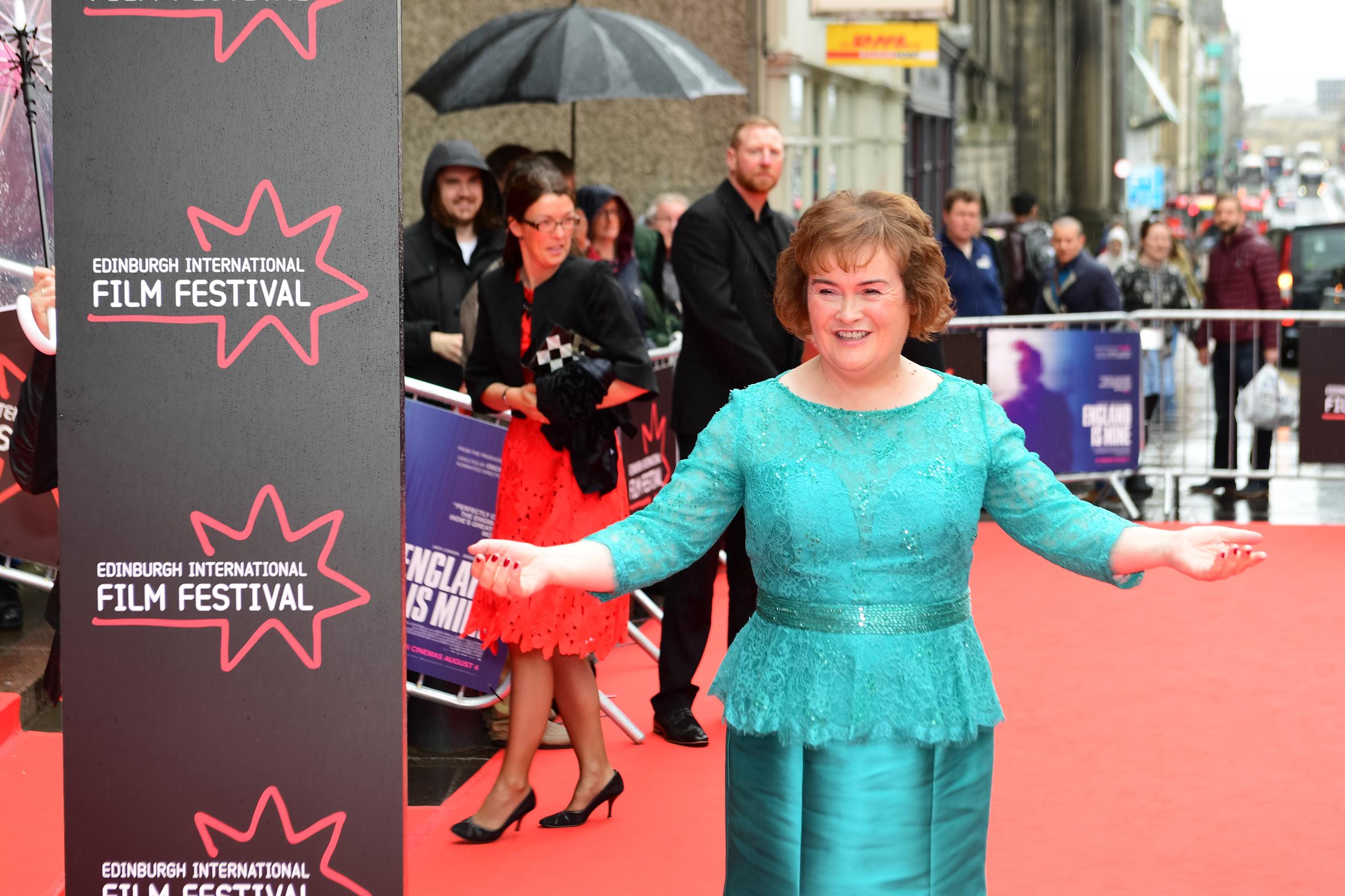 Boyle beams at the camera on the rain-soaked red carpet at the Edinburgh International Film Festival on 2 July 2017, fans straining against barriers and umbrellas dotting the crowd behind her, as she stands in a long-sleeved teal lace dress.
