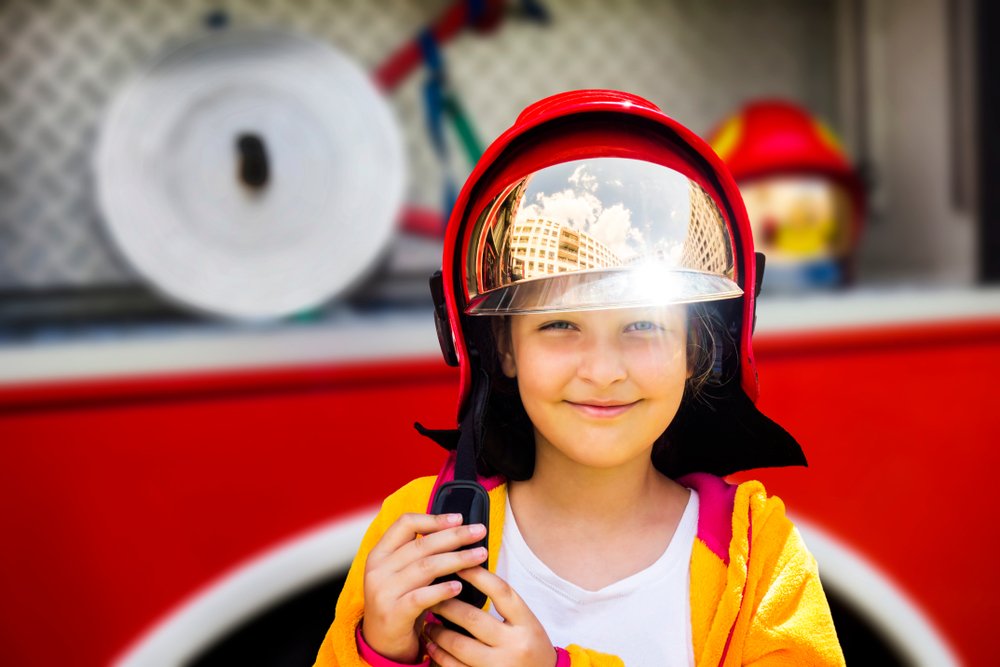 Young girl wearing a fireman's helmet and standing in front of a firetruck | Photo: Shutterstock