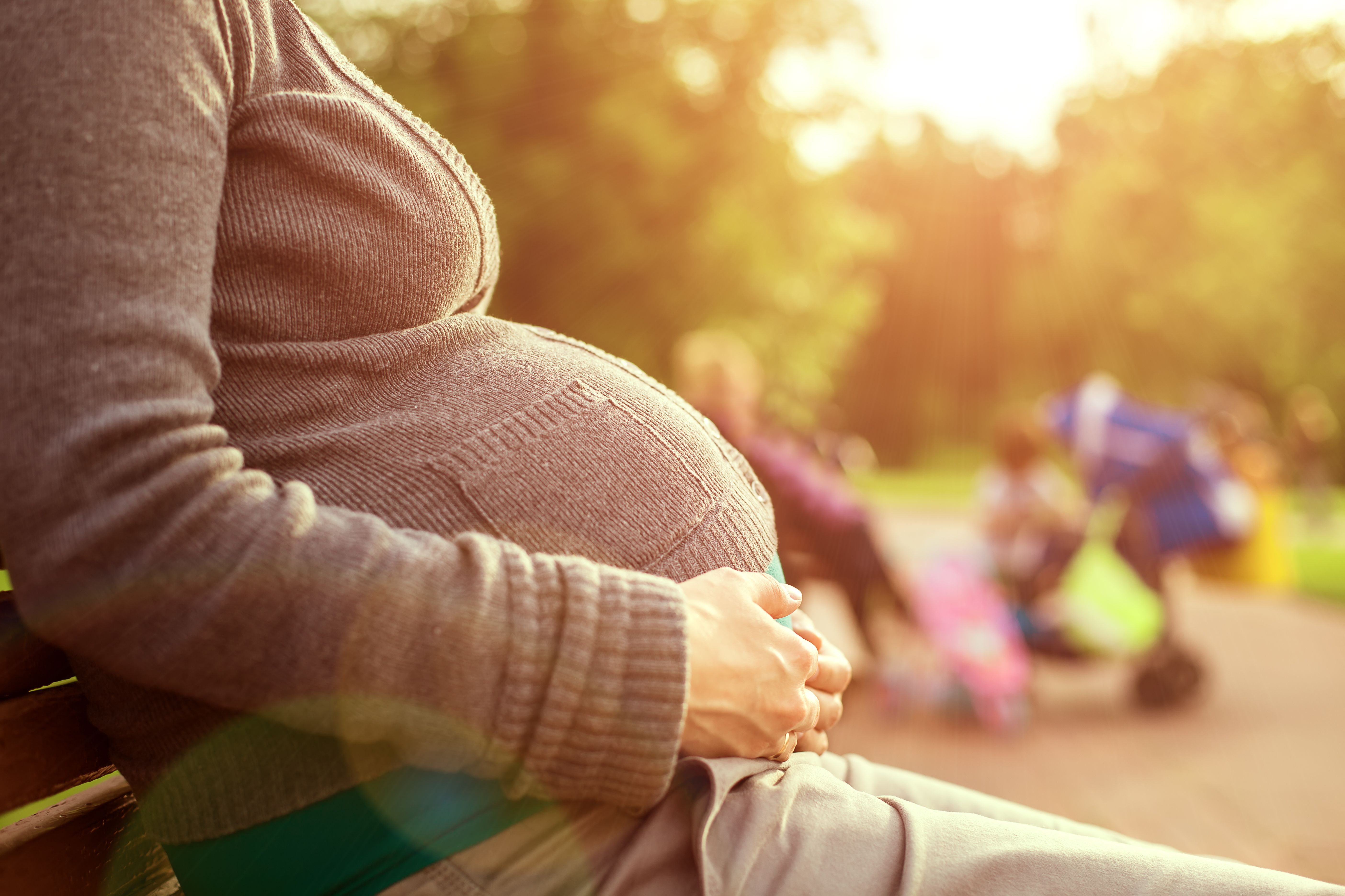 A pregnant woman in the park, holding her growing belly. | Source: Shutterstock