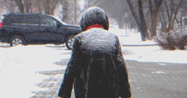 A person covered in snow walking towards a car | Source: Shutterstock