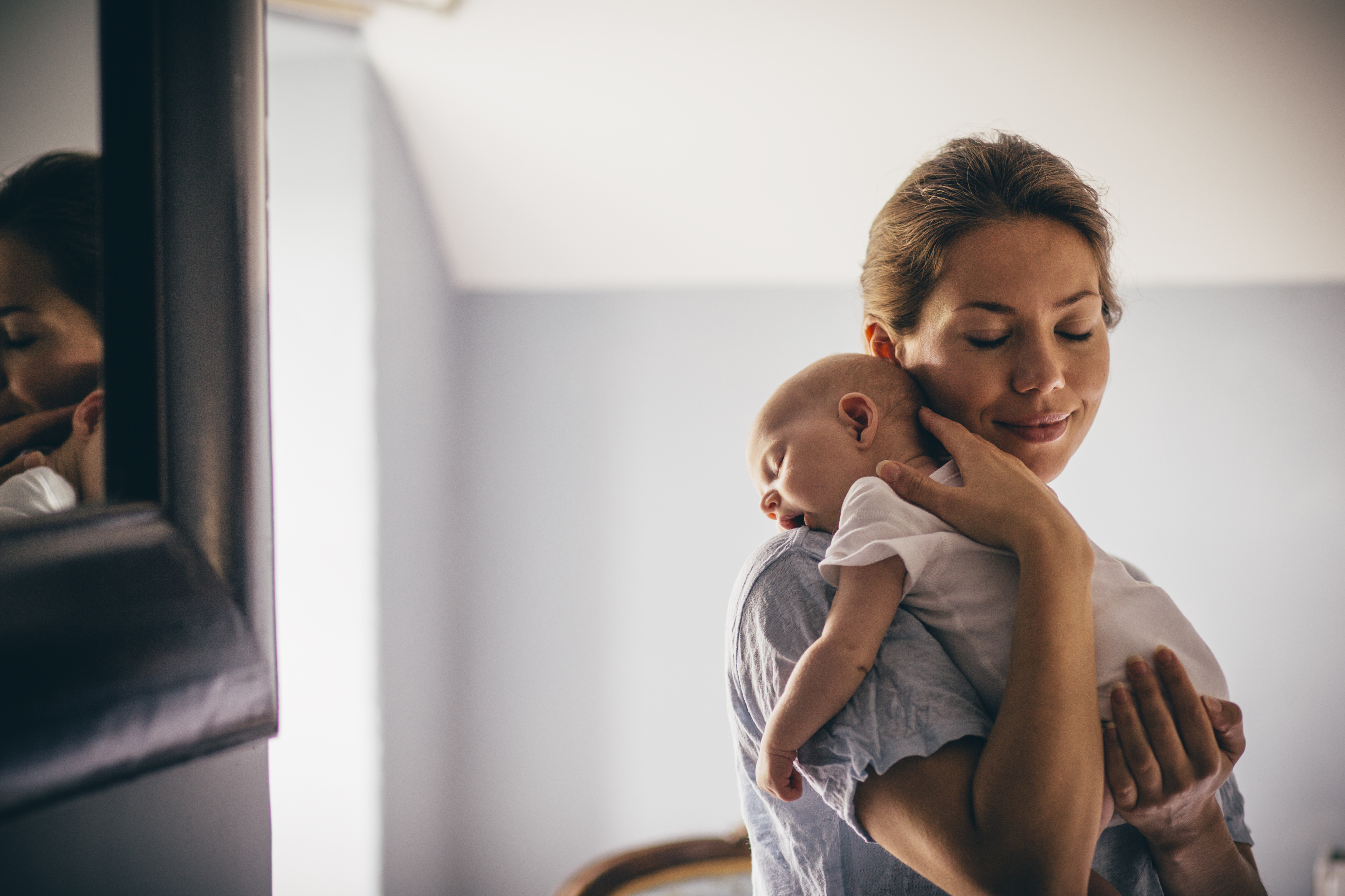 A happy new mother smiles as she cradles her sleeping baby in her arms. | Source: Getty Images