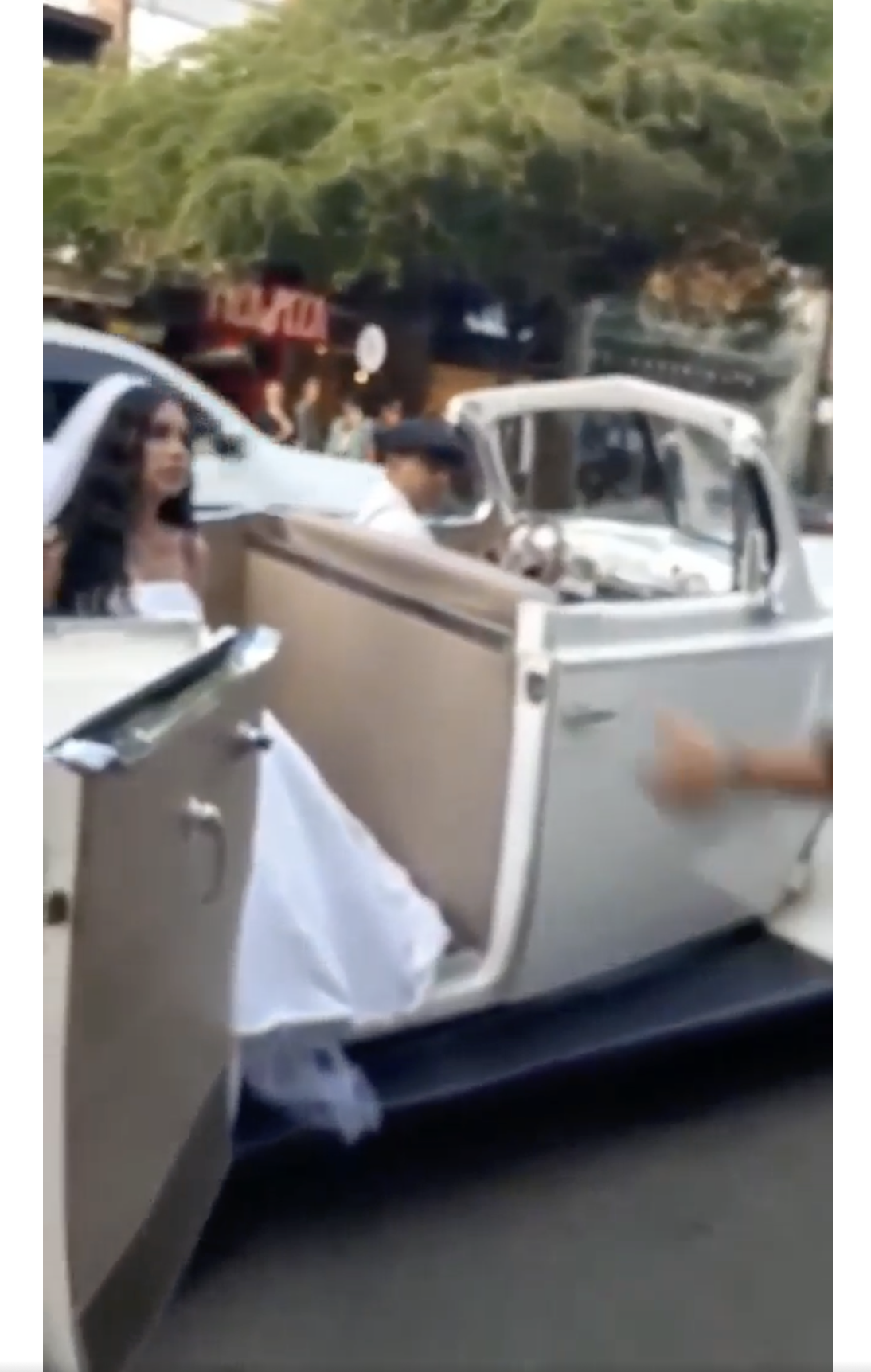 Eine Frau in einem weißen Brautkleid wird in einem klassischen Hochzeitsfahrzeug auf der Straße abgebildet. | Quelle: facebook.com/maspopulareventos