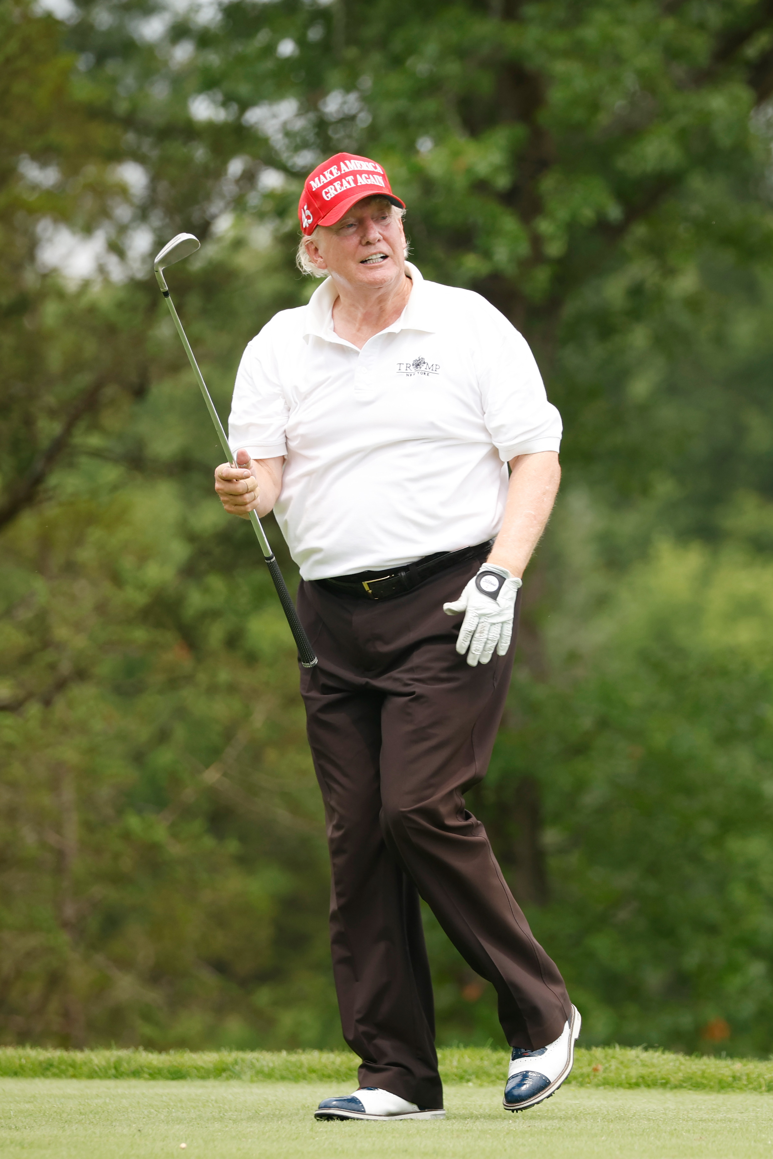 Donald Trump appears relaxed, mid-stride, holding a club with one hand while smiling slightly. The uneven skin tones are clear, especially around his chin and temples.