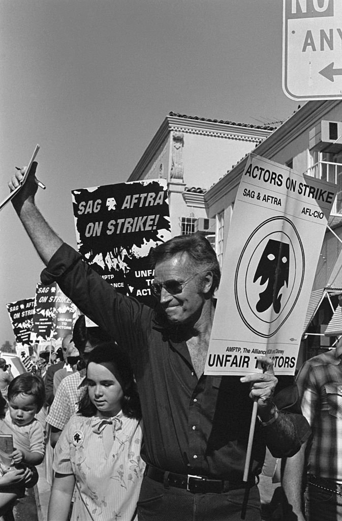 Charlton Heston waves as he carries his picket sign as members of the striking Screen Actors Guild picket Paramount Picture's studio | Photo: Getty Images