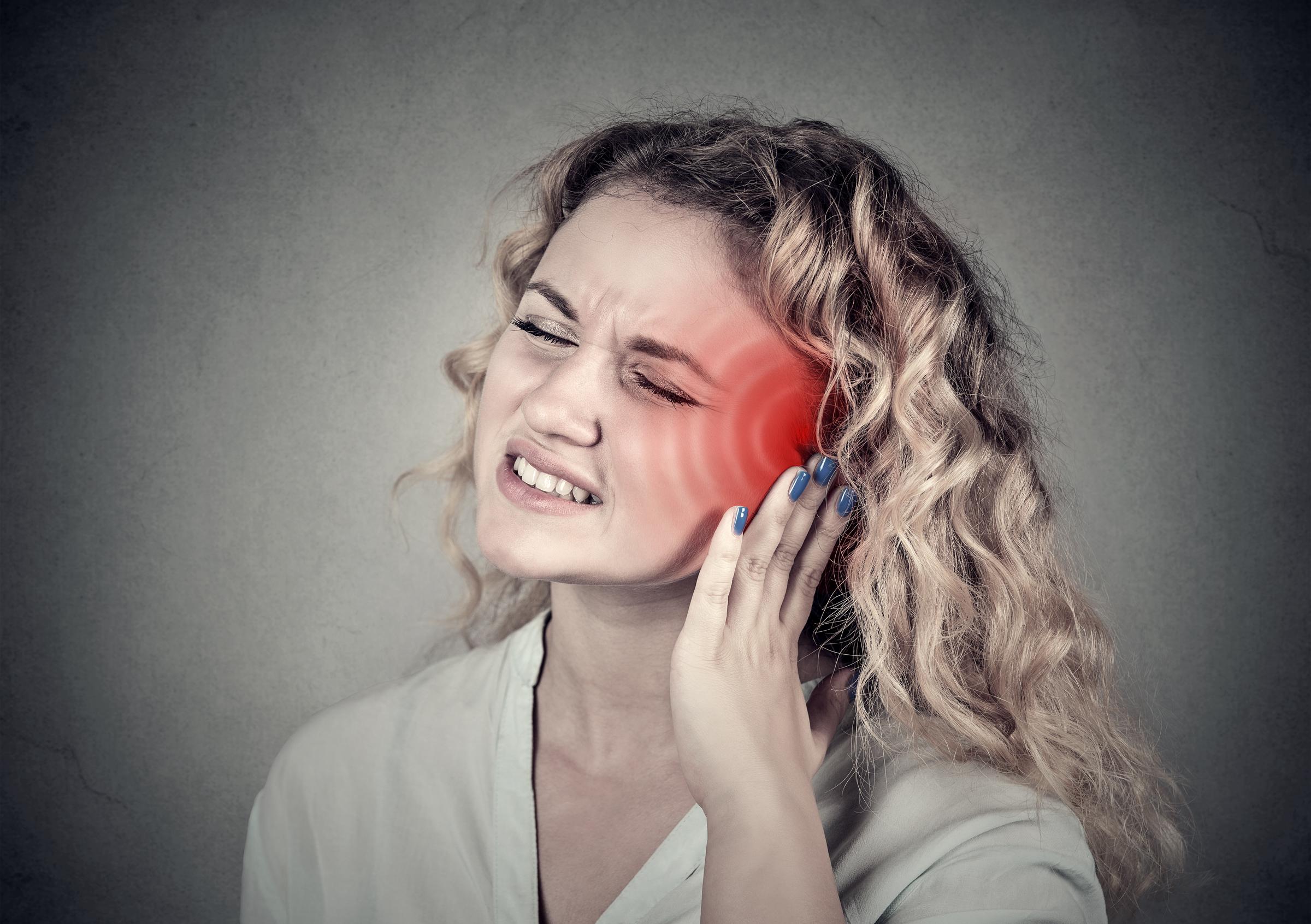 Woman holding her ear in discomfort, possibly experiencing tinnitus | Source: Getty Images